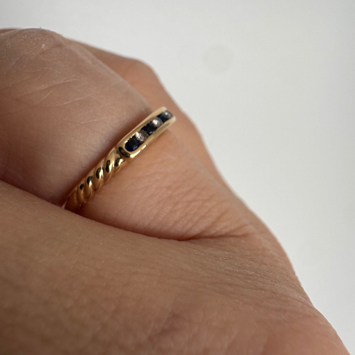 טבעת זהב צהוב 18 קראט בעיצוב נקי ומדויק, משובצת בשורה עדינה של אבני ספיר כחולות וביניהן יהלומים לבנים.