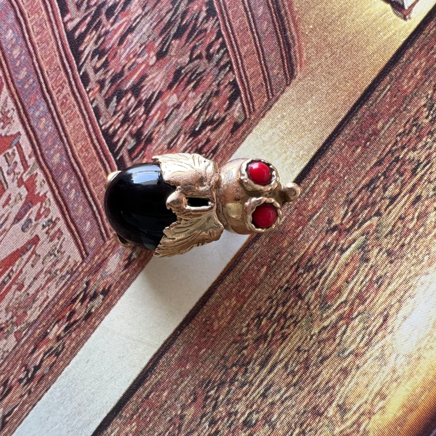 תליון בצורת חיפושית מזהב 14 קראט, עם עיניים אדומות מאבן קורל בחיתוך קבושון וגוף מאבן אוניקס שחורה מבריקה.