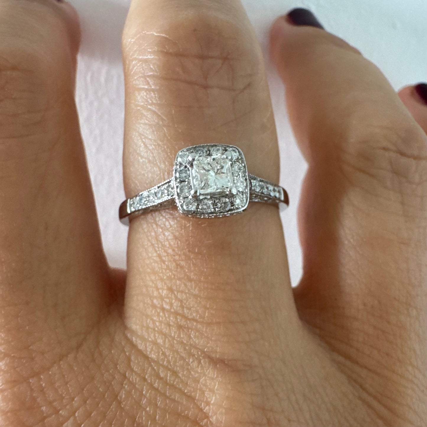 טבעת זהב לבן 14 קראט משובצת יהלום מרכזי בחיתוך פרינסס, מוקף הילת יהלומים קטנים וזרוע משובצת פאווה