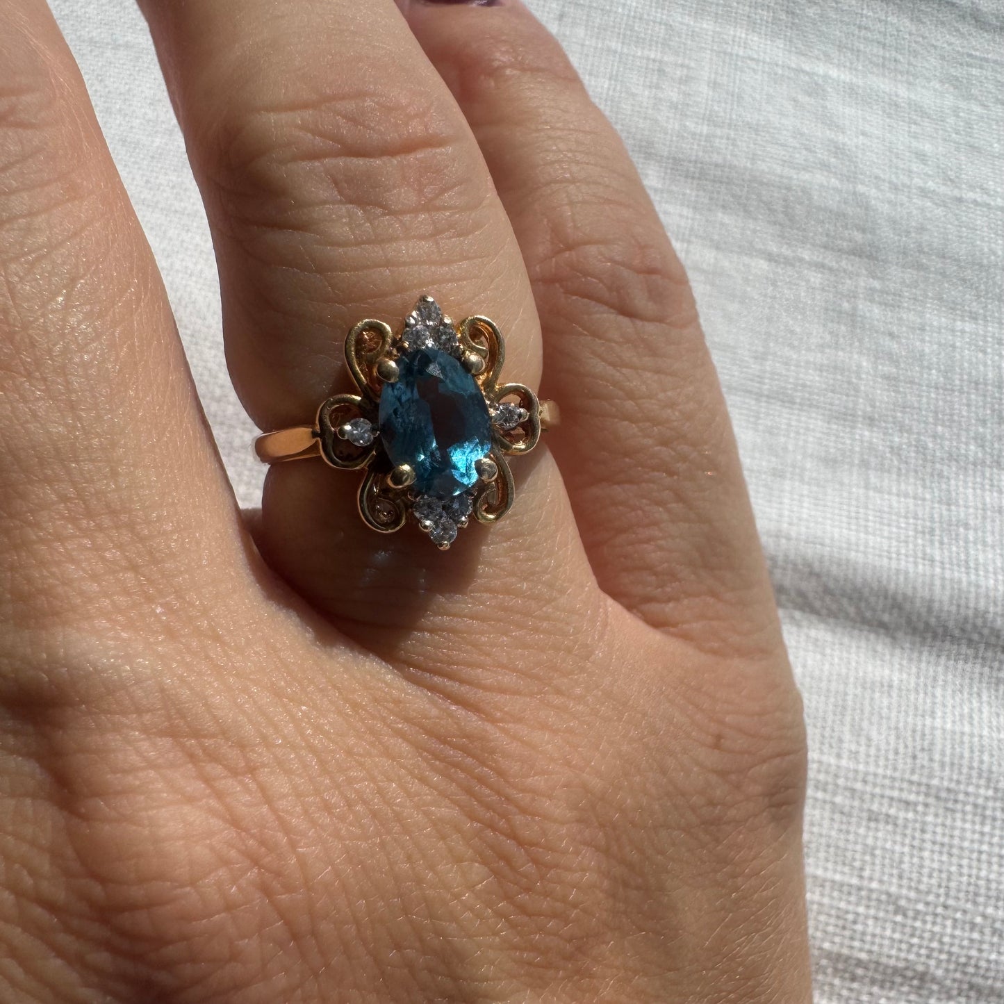 18K gold ring featuring an oval-cut Blue Topaz at the center, accented by sparkling side Diamonds and elegant scroll details.