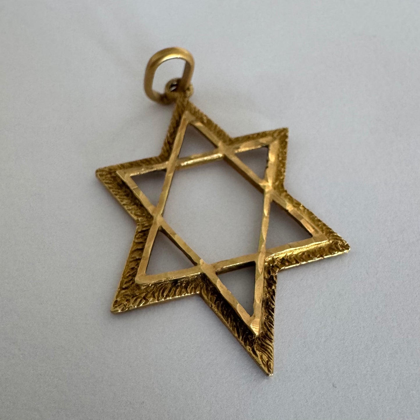 תליון מגן דוד מזהב צהוב 14 קראט בעיצוב פתוח, עם טקסטורה עדינה בשוליים המוסיפה עומק ואופי.