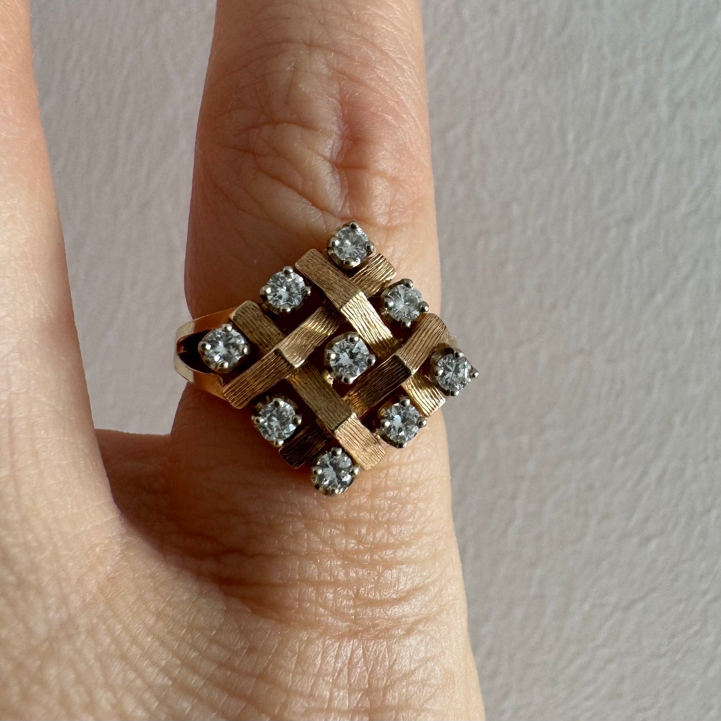 טבעת זהב צהוב 14 קראט בעיצוב קלוע וגאומטרי, משובצת יהלומים עגולים בפריסה סימטרית.