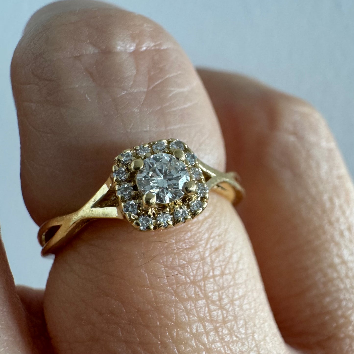 טבעת זהב 14 קראט משובצת יהלום מרכזי עגול ומבריק, מוקף הילה עדינה של יהלומים המעצימים את הברק