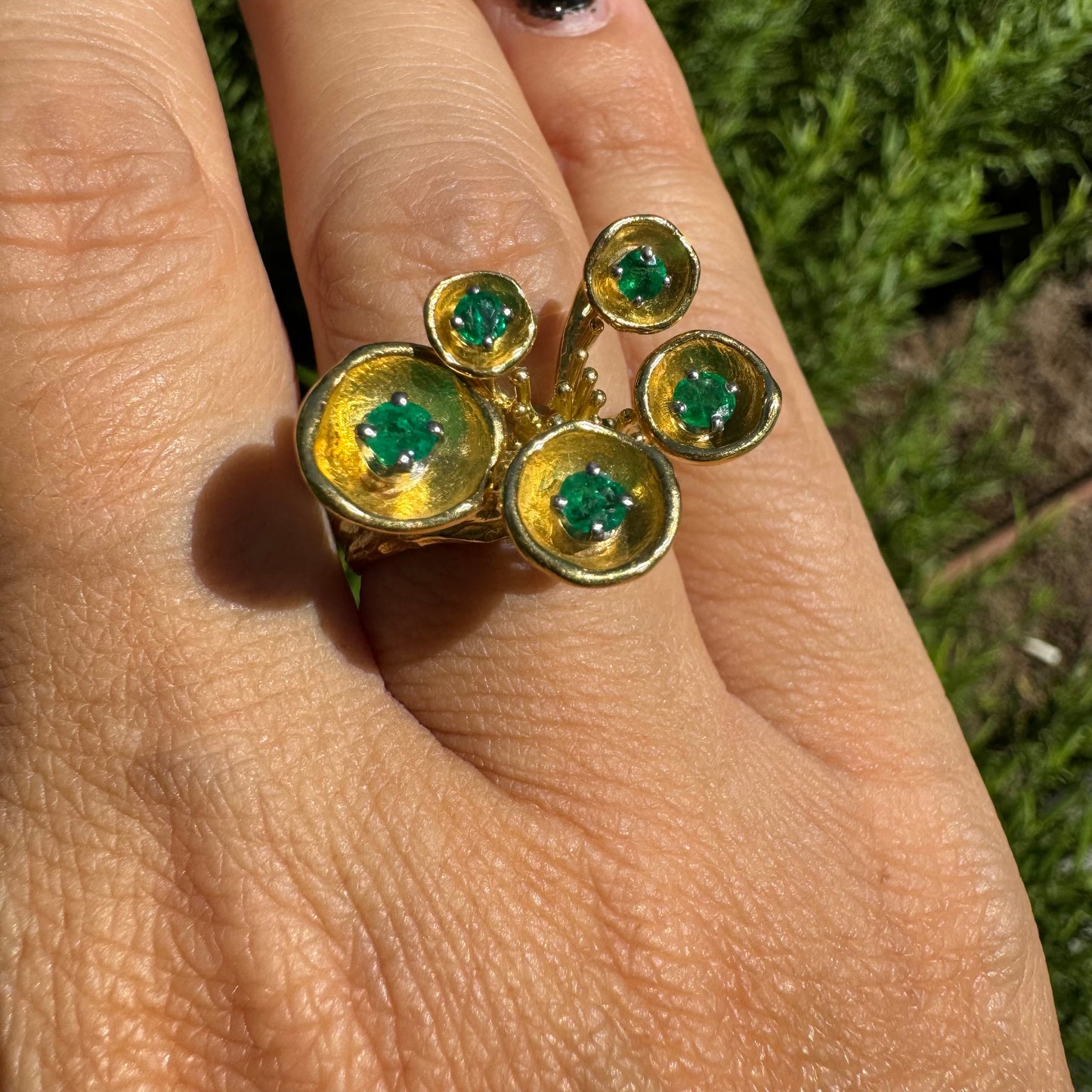 18K gold ring with an artistic floral-inspired design, set with round Emerald in textured circular settings.
