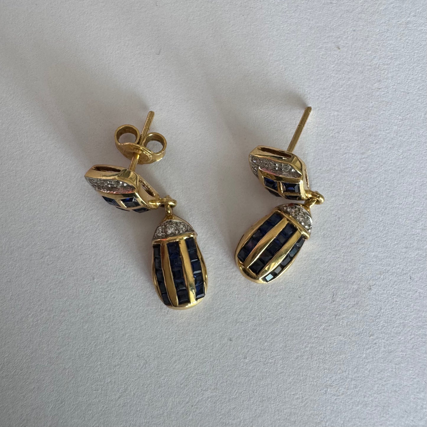 עגילי זהב צהוב 18 קראט תלויים, משובצים אבני ספיר כחולות בגוון כחול עמוק בעיצוב גיאומטרי, בשילוב יהלומים מנצנצים
