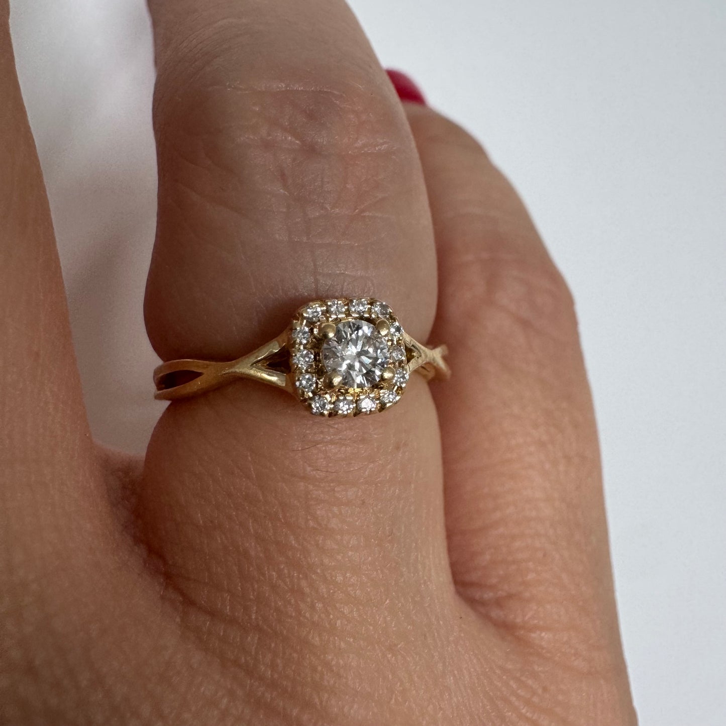 טבעת זהב 14 קראט משובצת יהלום מרכזי עגול ומבריק, מוקף הילה עדינה של יהלומים המעצימים את הברק