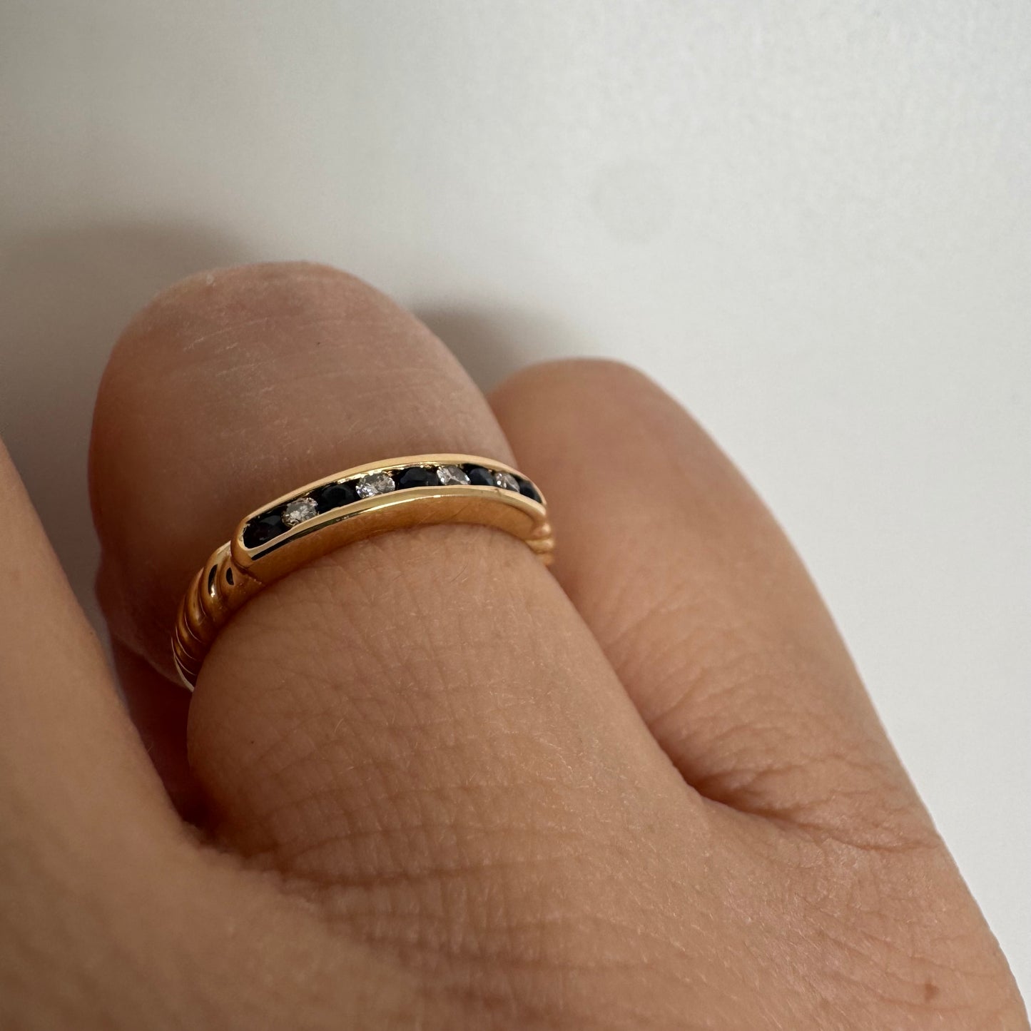 טבעת זהב צהוב 18 קראט בעיצוב נקי ומדויק, משובצת בשורה עדינה של אבני ספיר כחולות וביניהן יהלומים לבנים.