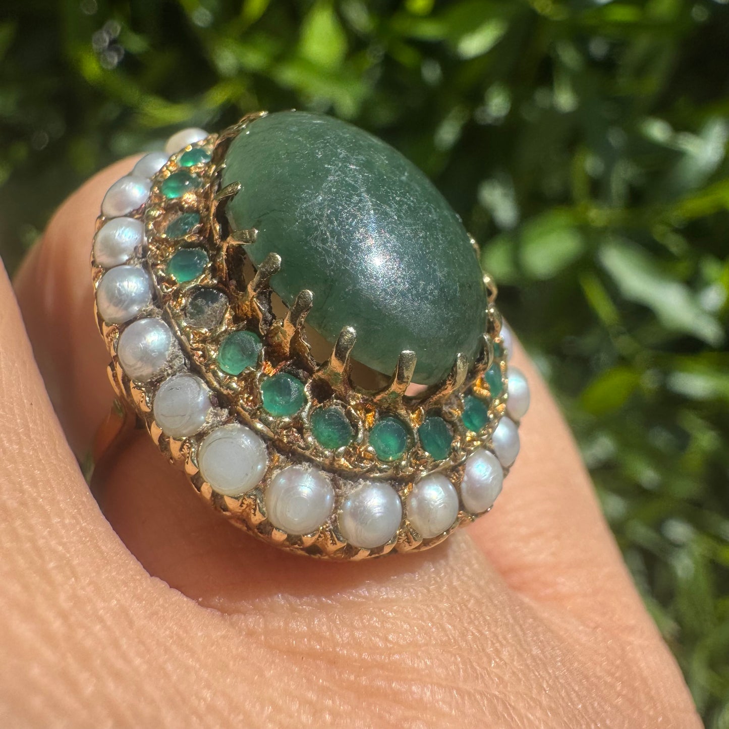 14K gold set with a large oval green Jade at its center, surrounded by concentric halos of sparkling Emeralds and delicate pearls