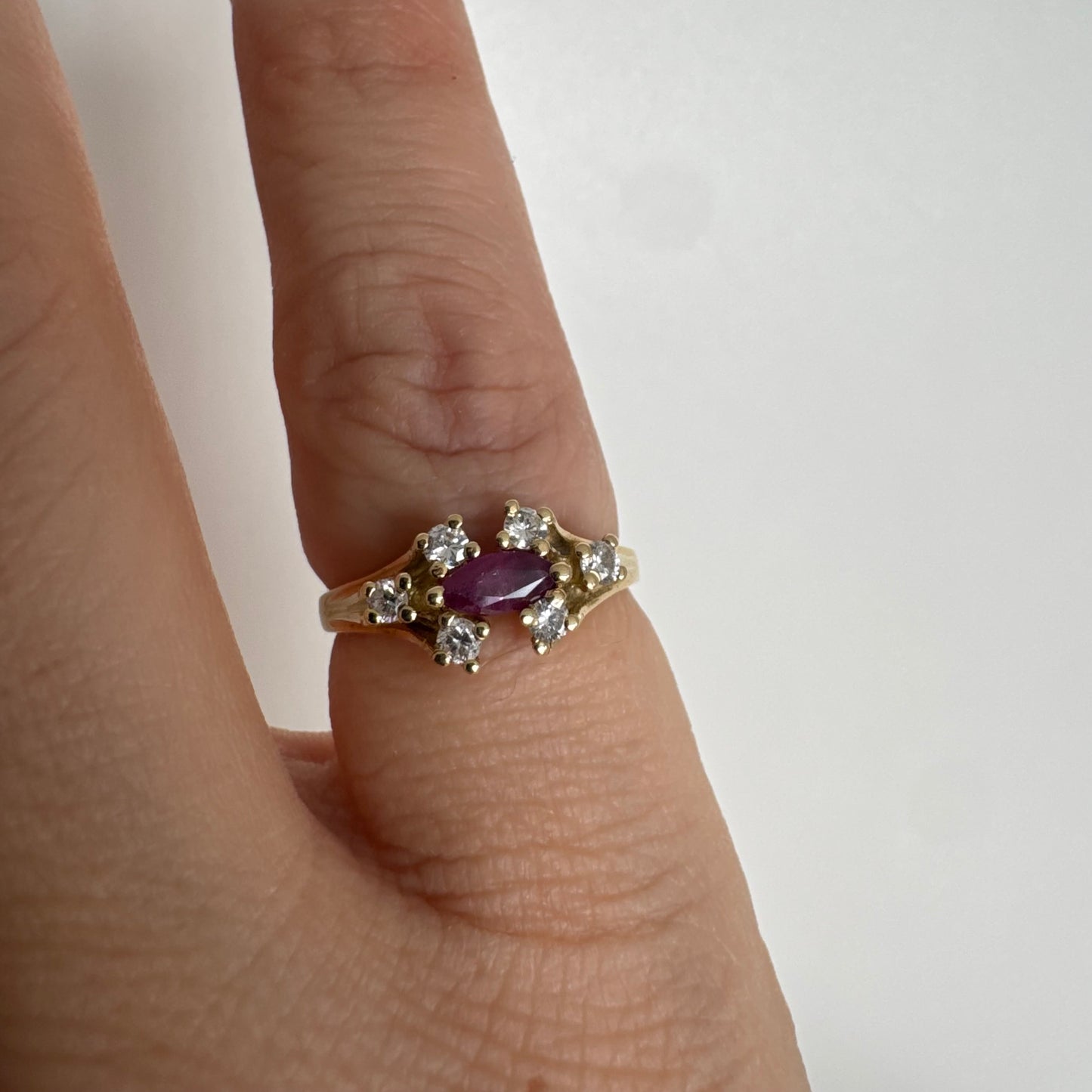 טבעת זהב צהוב 18 קראט משובצת אבן רובי בחיתוך מרקיזה בגוון מוקפת יהלומים בחיתוך עגול משני הצדדים.