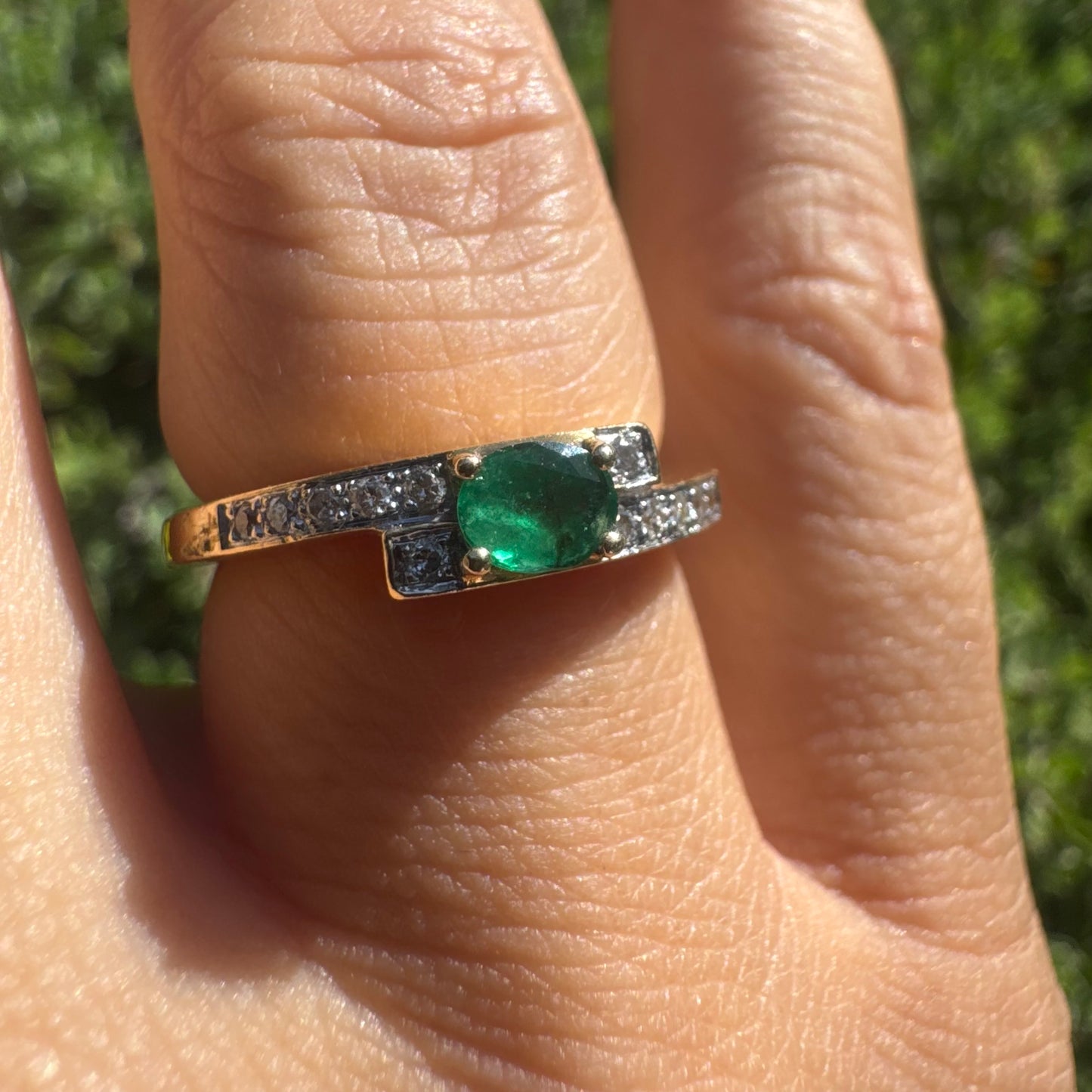 18K gold ring set with an oval green Emerald at the center, accented with sparkling Diamonds along the band.