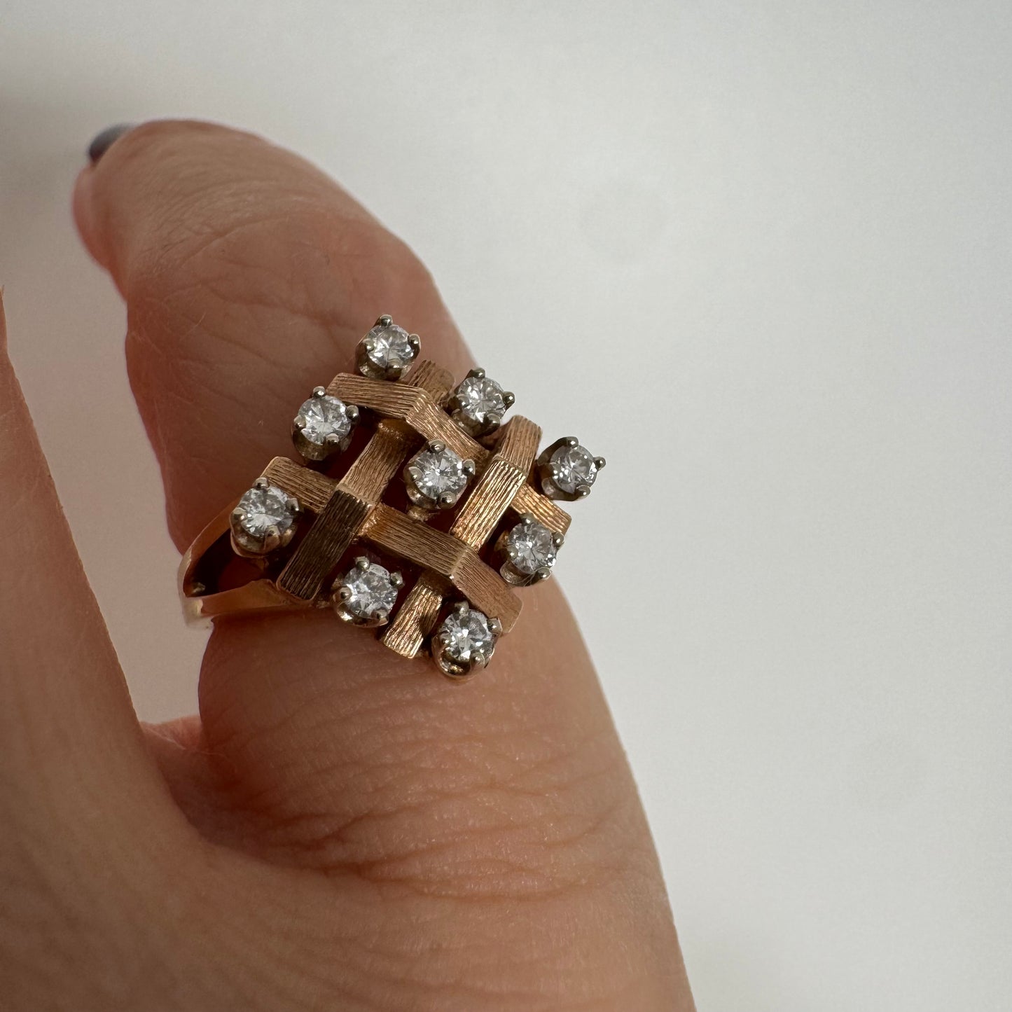 טבעת זהב צהוב 14 קראט בעיצוב קלוע וגאומטרי, משובצת יהלומים עגולים בפריסה סימטרית.