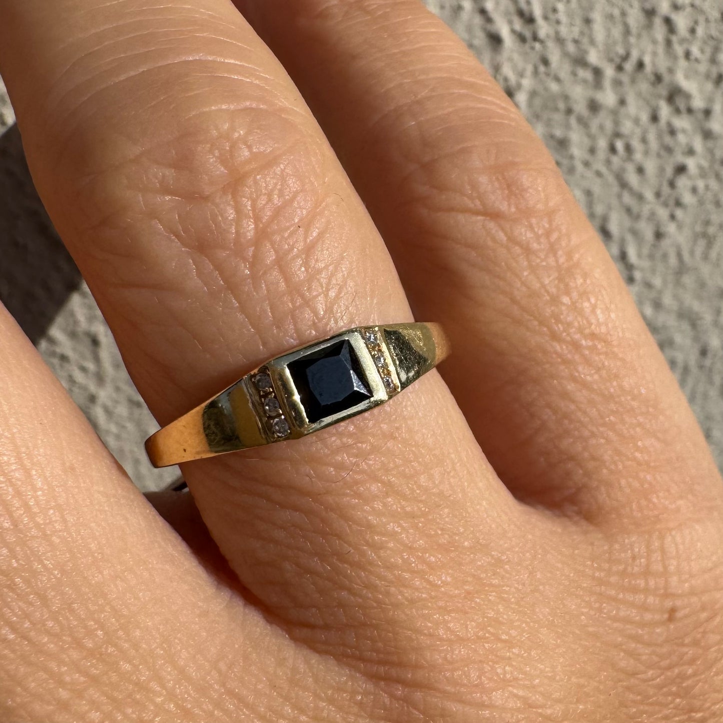 טבעת זהב 14 קראט משובצת אבן ספינל שחור בחיתוך ריבועי במרכז ויהלומים קטנים משני הצדדים.
