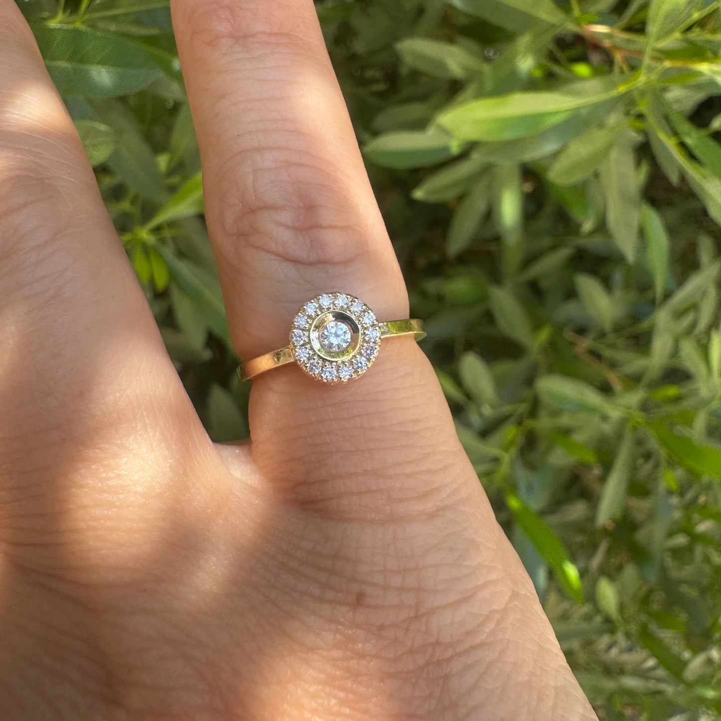 14K gold ring set with a bezel-set central Diamond, surrounded by a sparkling halo of brilliant-cut Diamonds.
