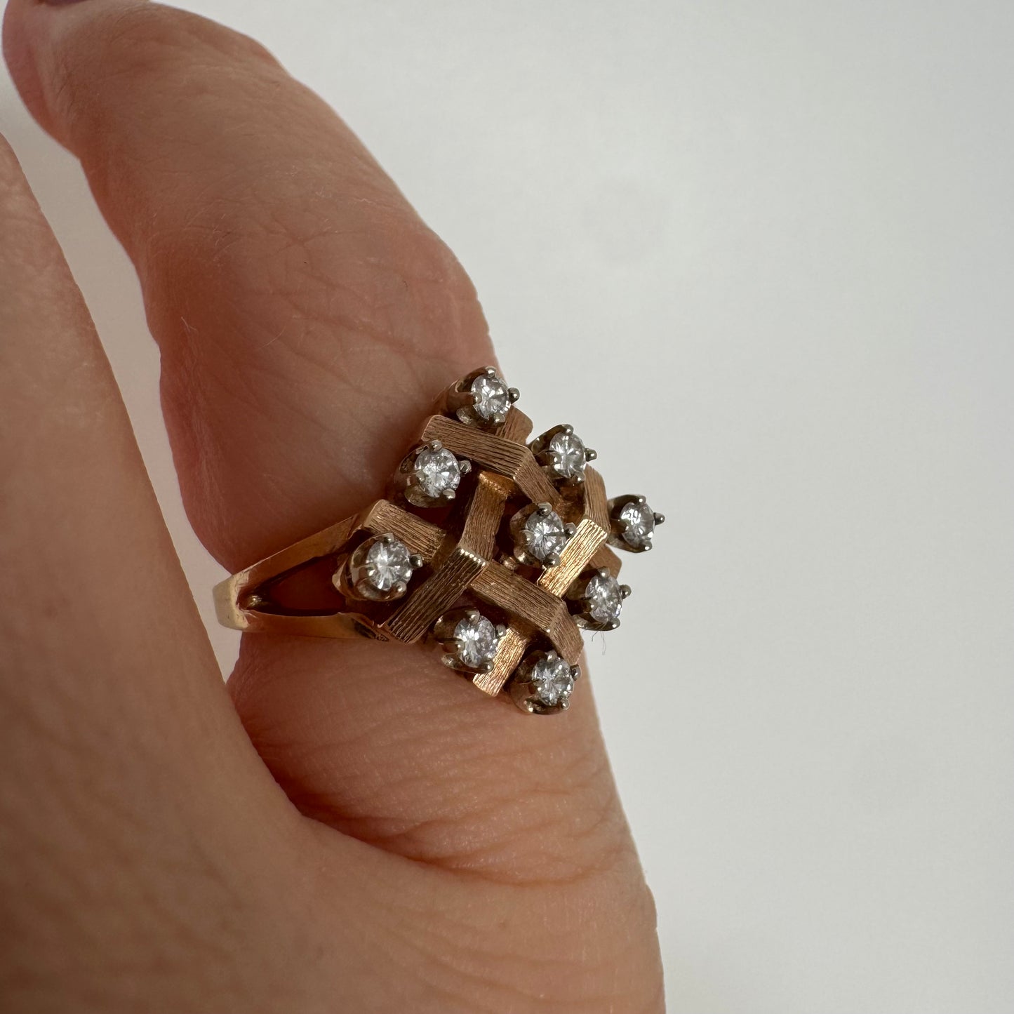 טבעת זהב צהוב 14 קראט בעיצוב קלוע וגאומטרי, משובצת יהלומים עגולים בפריסה סימטרית.