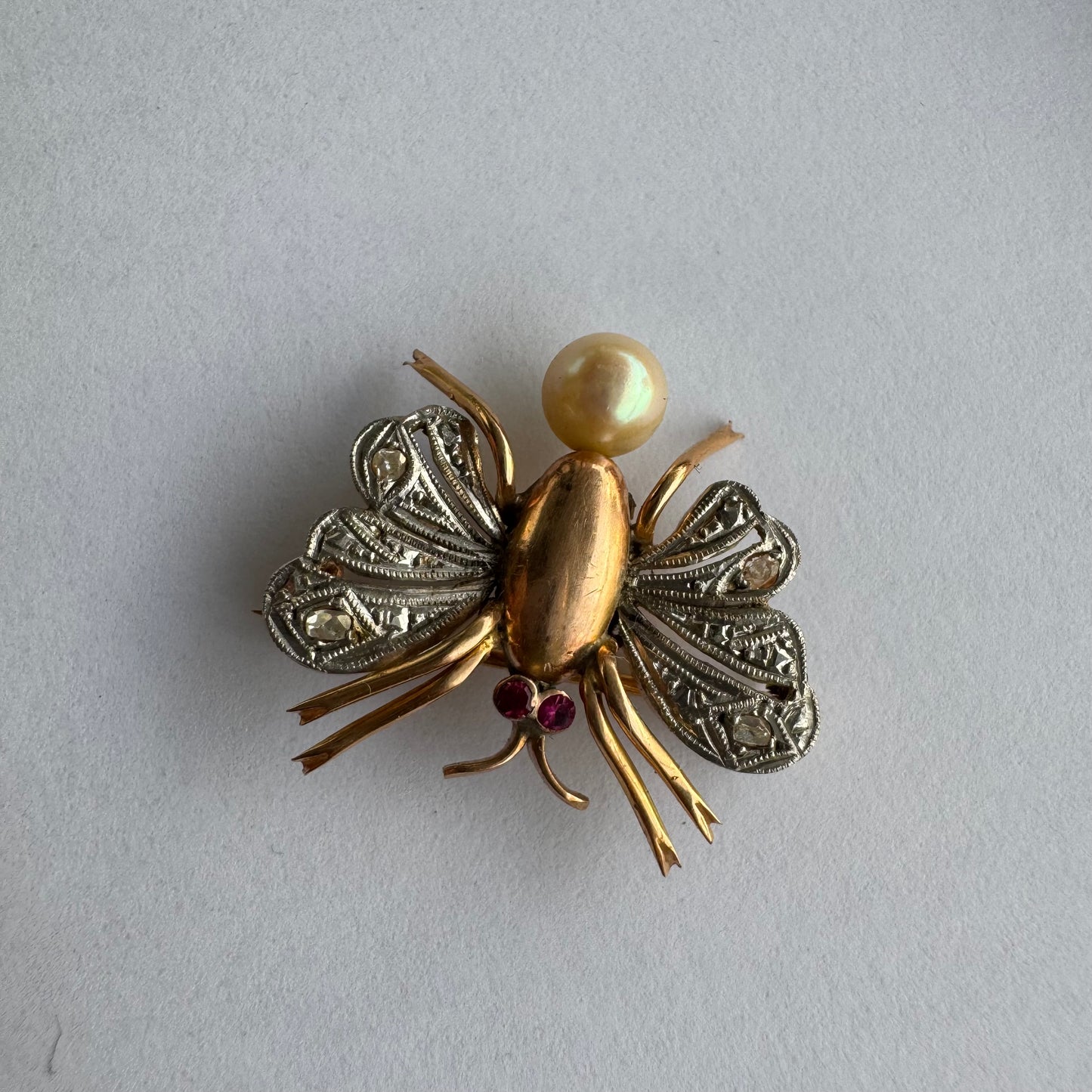 סיכת חרק ייחודית עשויה זהב 14 קראט משובצת יהלומים בעבודת פיליגרן עדינה בכנפיים, אבני רובי אדומות בעיניים ופנינה טבעית בגוון שמפניה.