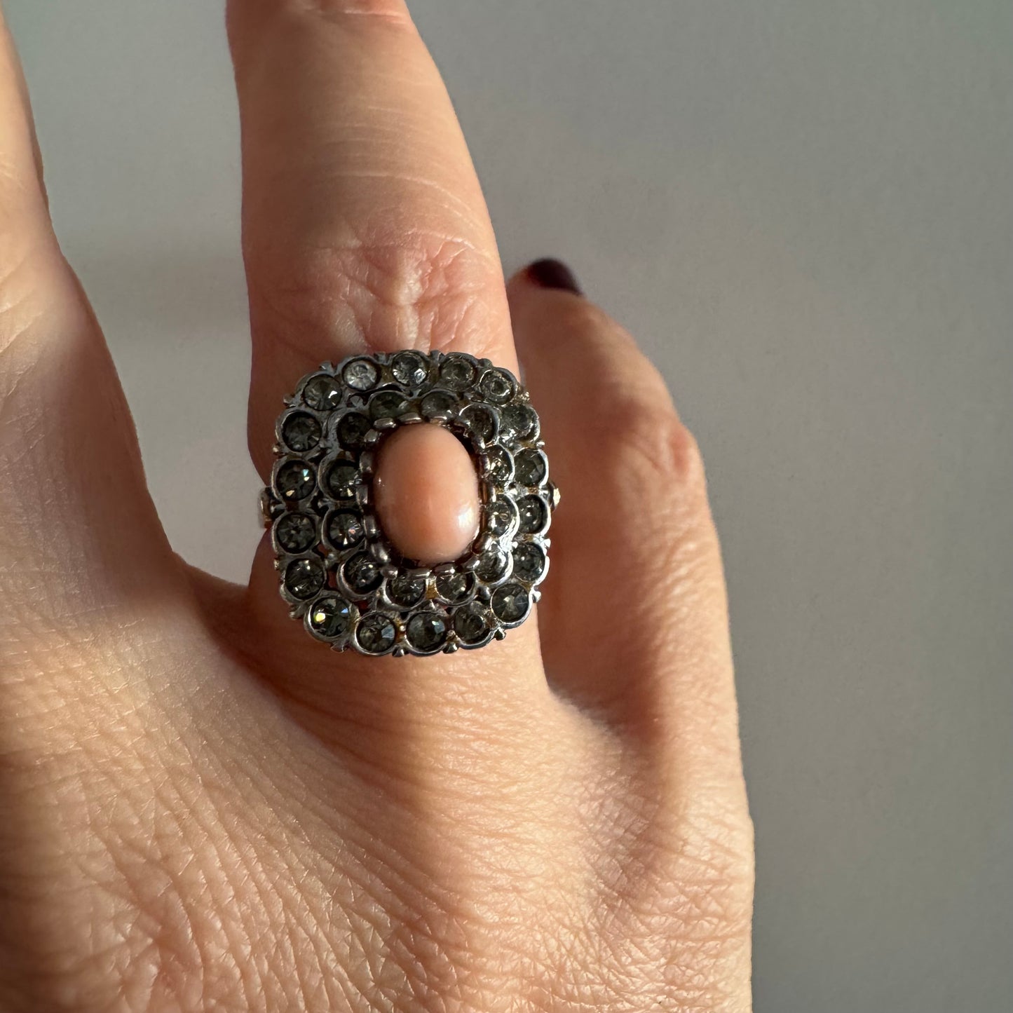 טבעת וינטג׳ עם חלק תחתון מזהב 14 קראט וחלק עליון עשוי כסף משובצת אבן קורל בהירה במרכז ומסביבה אבנים בהירות שאינן יהלומים.