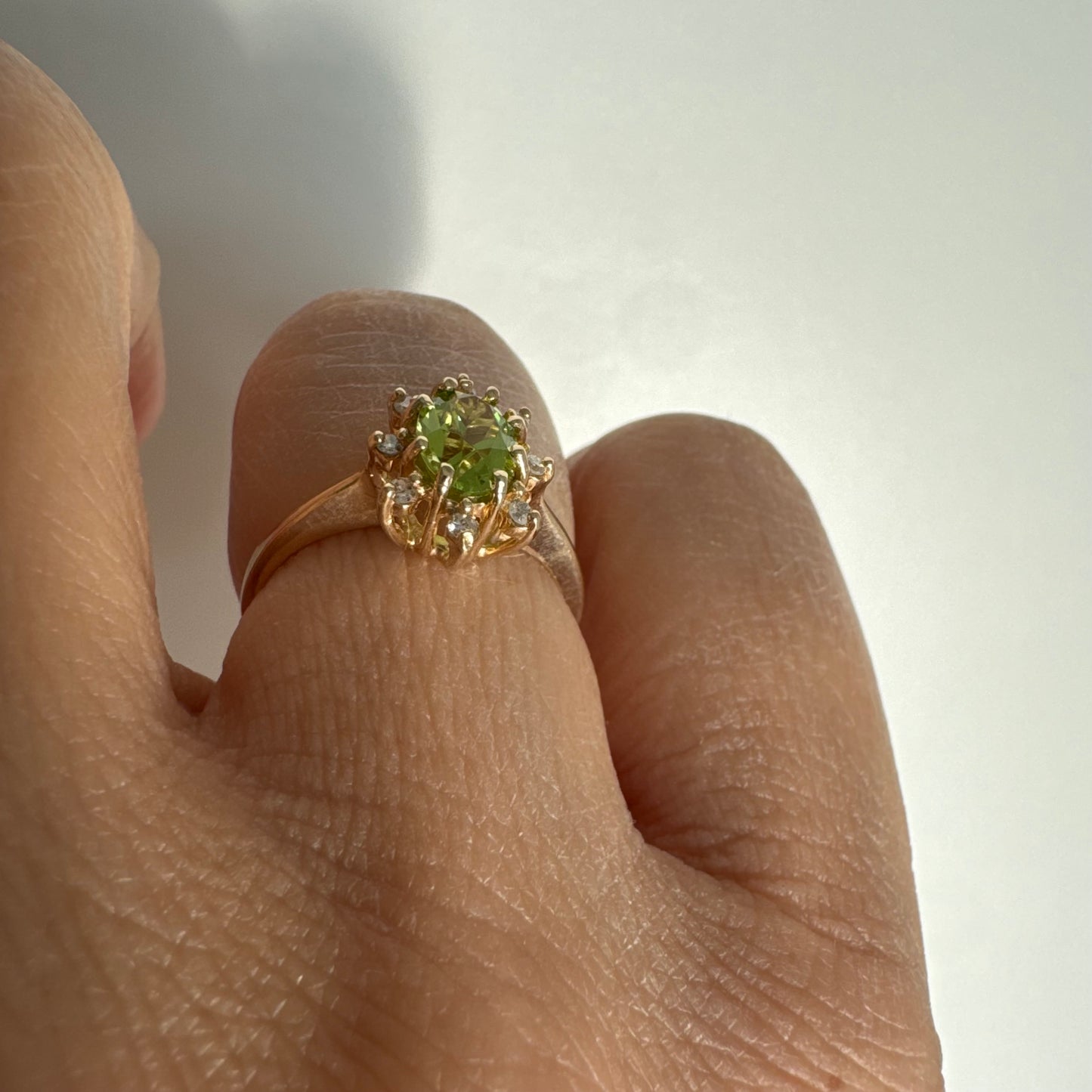 טבעת זהב 14 קראט משובצת אבן פרידוט ירוקה בחיתוך אובלי, מוקפת יהלומים היוצרים הילה עדינה מסביבה.