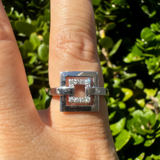 טבעת זהב לבן 18 קראט בעיצוב גאומטרי, הכוללת שני מסגרות ריבועיות פתוחות, כשהריבוע הפנימי משובץ יהלומים נוצצים.