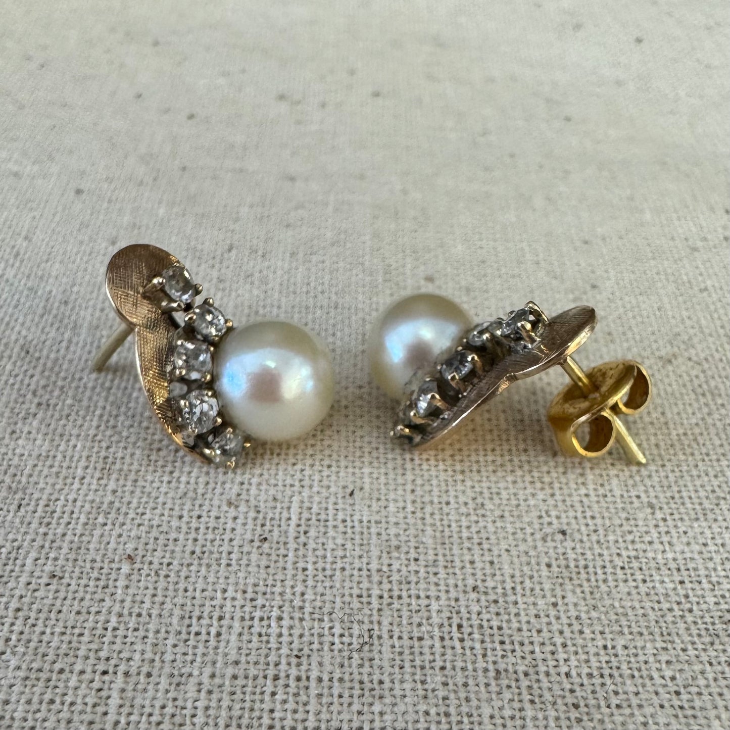 עגילי זהב צהוב 14 קראט, צמודים לאוזן, עשויים זהב בגימור טקסטורלי ומשובצים פנינה עגולה ובשורת יהלומים קטנים בחיתוך עתיק.