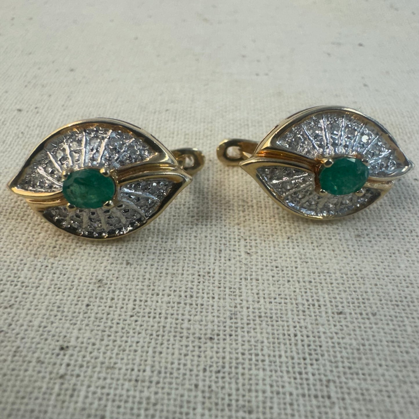 עגילים צמודים לאוזן, זהב צהוב 14 קראט, משובצים אמרלד במרכז, וסביבן פיתוחים משובצים יהלומים, שמעניקים מראה של ניצוץ רך ואלגנטי