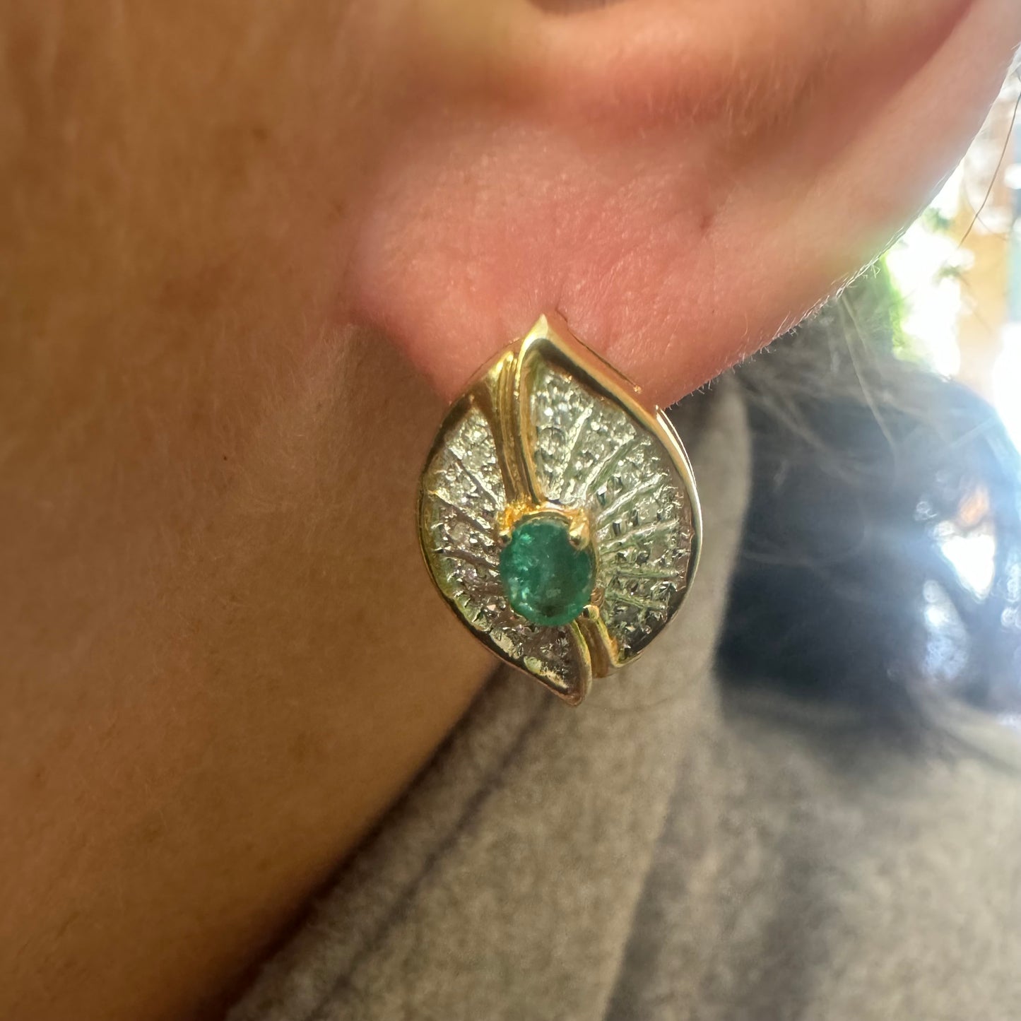 עגילים צמודים לאוזן, זהב צהוב 14 קראט, משובצים אמרלד במרכז, וסביבן פיתוחים משובצים יהלומים, שמעניקים מראה של ניצוץ רך ואלגנטי