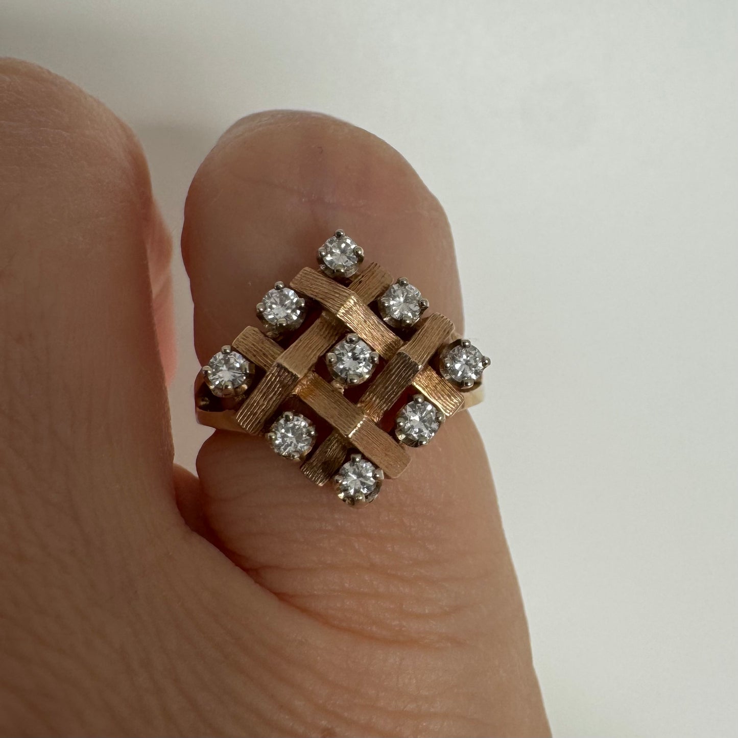 טבעת זהב צהוב 14 קראט בעיצוב קלוע וגאומטרי, משובצת יהלומים עגולים בפריסה סימטרית.