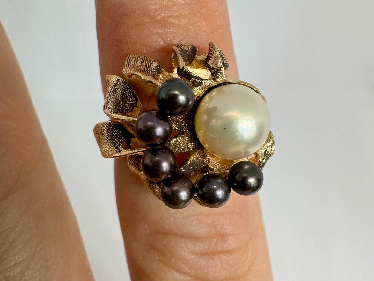 14K gold ring set with a luminous white Pearl at its center surrounded by a delicate circle of black Pearls.