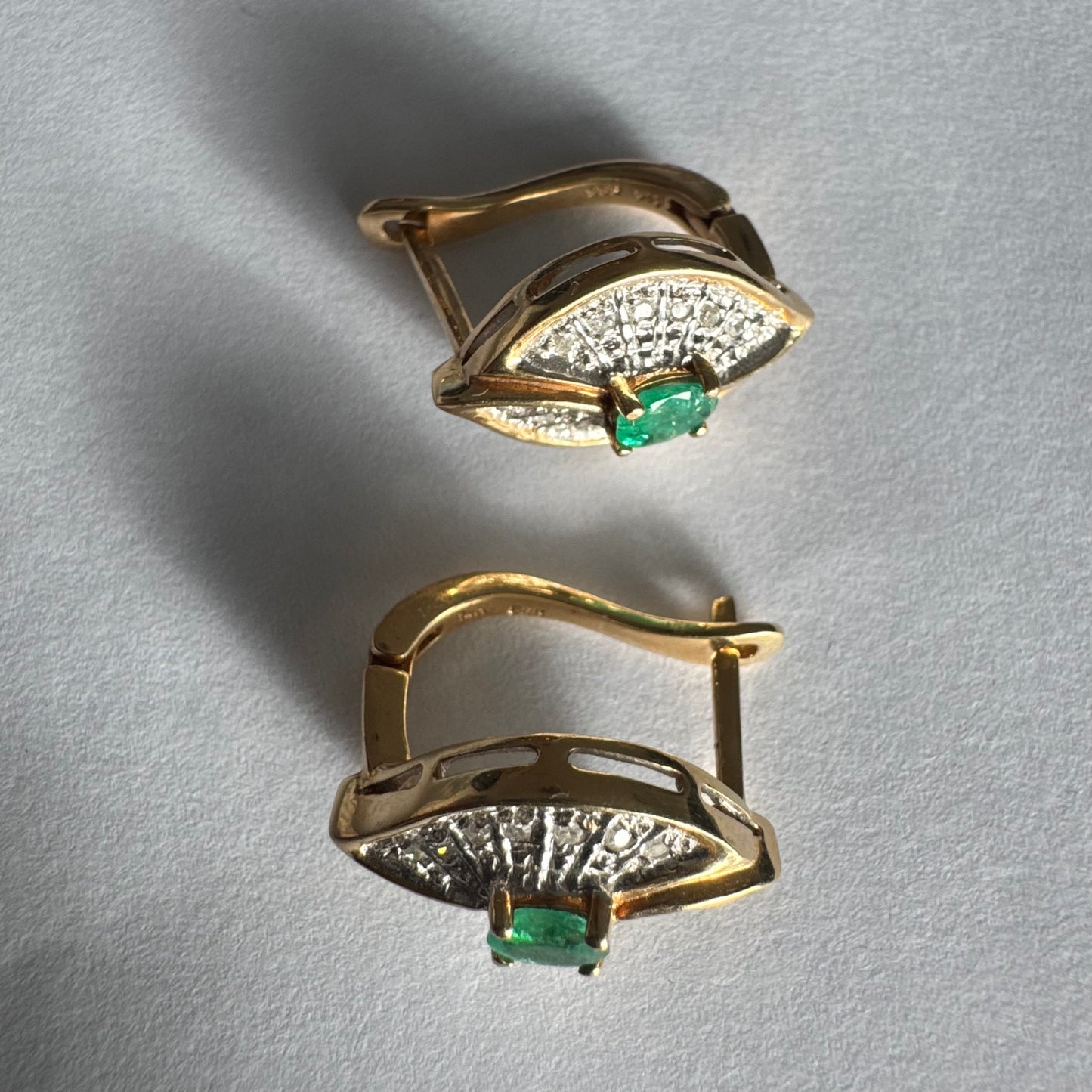 עגילים צמודים לאוזן, זהב צהוב 14 קראט, משובצים אמרלד במרכז, וסביבן פיתוחים משובצים יהלומים, שמעניקים מראה של ניצוץ רך ואלגנטי