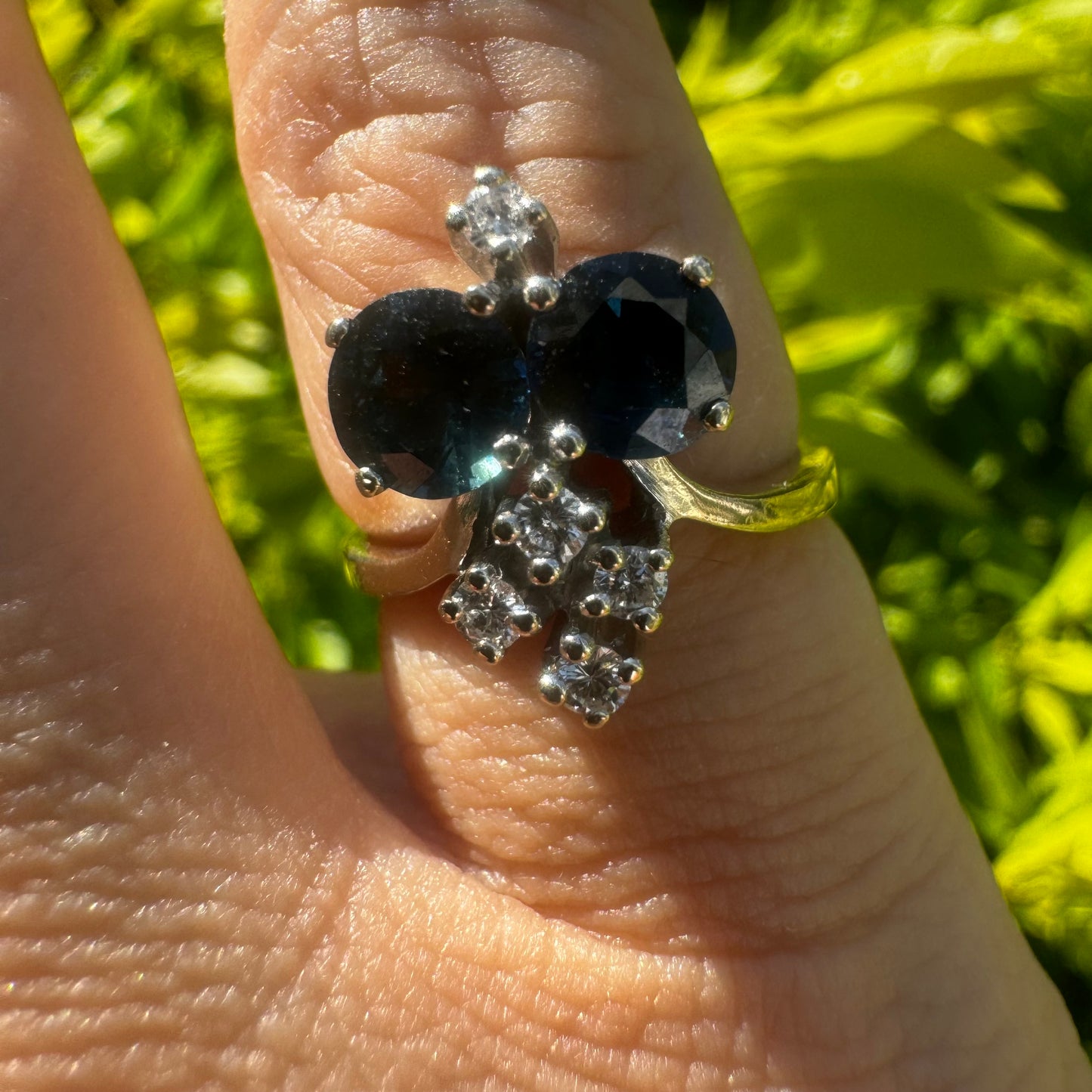 14K gold ring set with two deep blue oval Sapphires accented by clusters of brilliant white Diamonds.