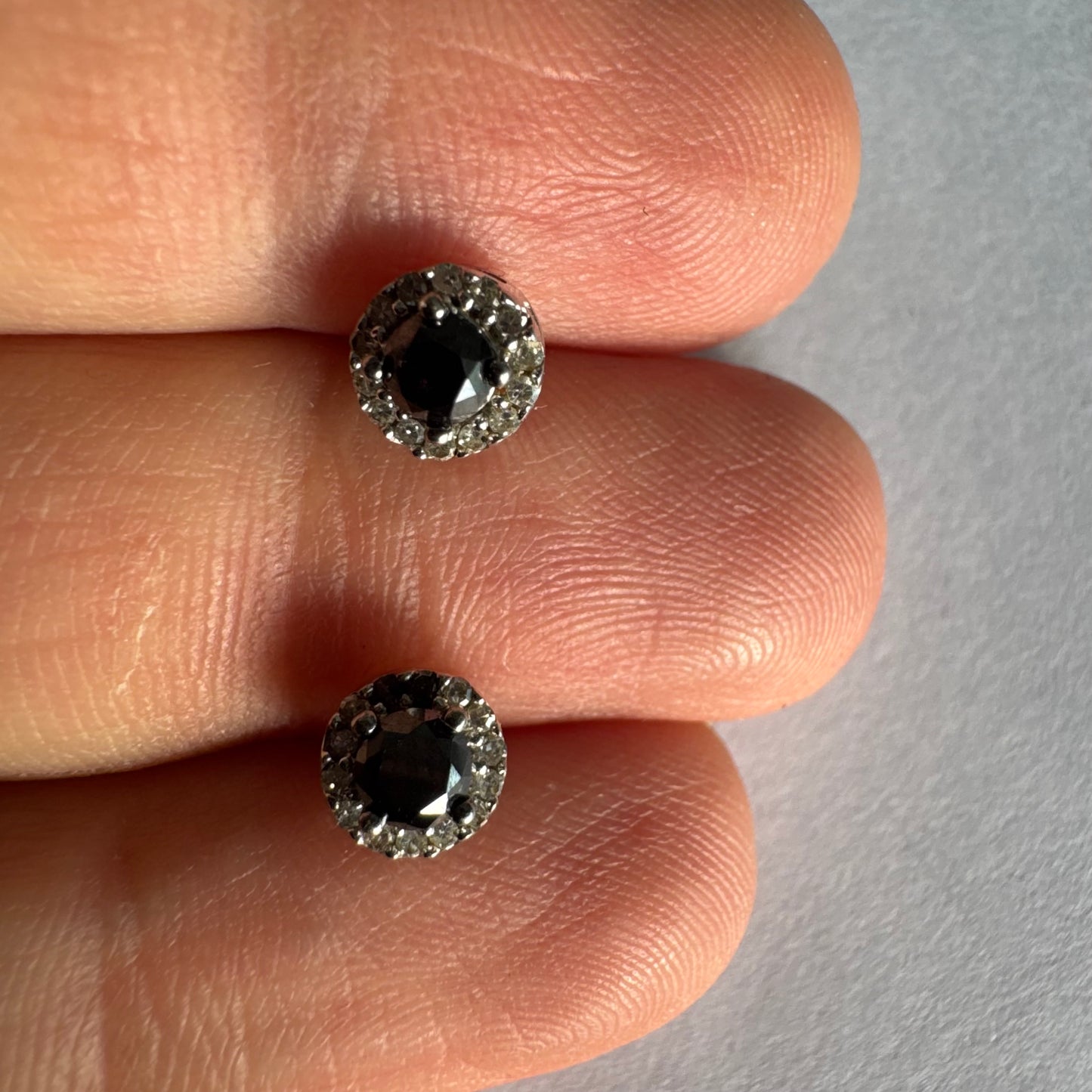 עגילי זהב לבן 10 קראט צמודים לאוזן, משובצים יהלומים שחורים עגולים במרכז ומסביבם הילה של יהלומים לבנים מנצנצים.