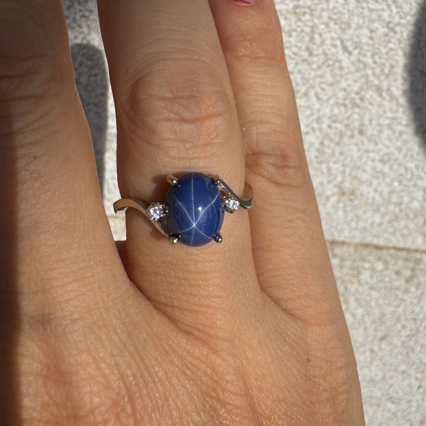 טבעת זהב לבן 14 קראט משובצת אבן ספיר כוכב מרהיבה, המציגה תופעת טבע של שישה קווים זוהרים, ובצידיה שני יהלומים מנצנצים. 