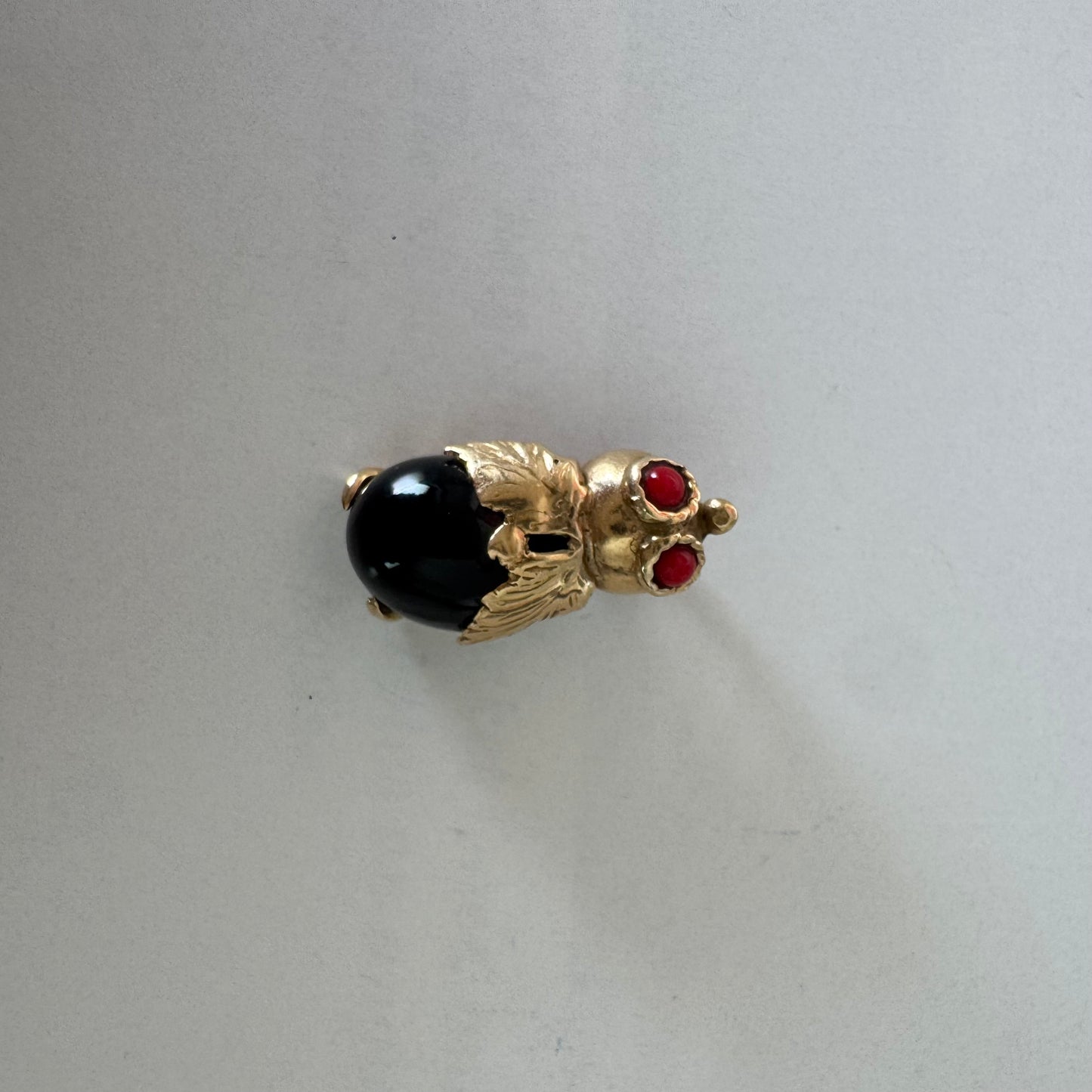 תליון בצורת חיפושית מזהב 14 קראט, עם עיניים אדומות מאבן קורל בחיתוך קבושון וגוף מאבן אוניקס שחורה מבריקה.