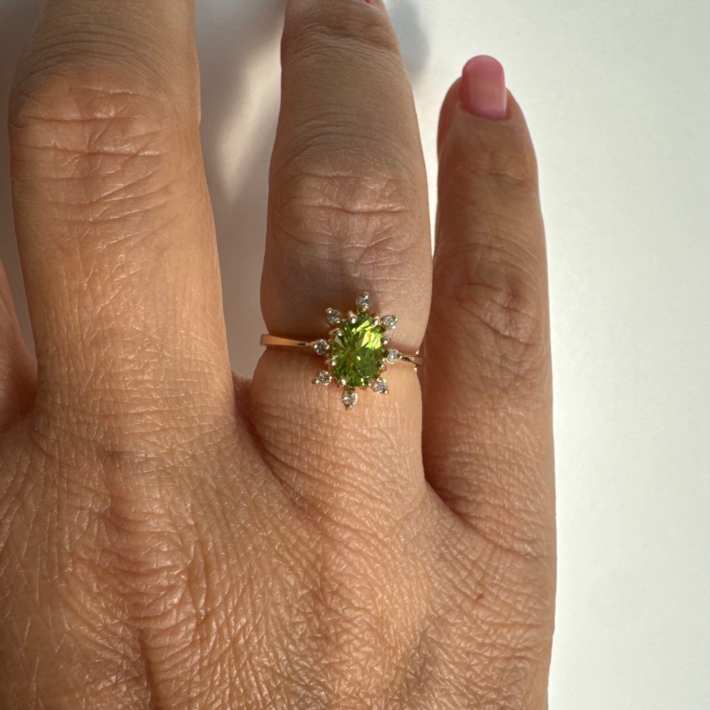 טבעת זהב 14 קראט משובצת אבן פרידוט ירוקה בחיתוך אובלי, מוקפת יהלומים היוצרים הילה עדינה מסביבה.