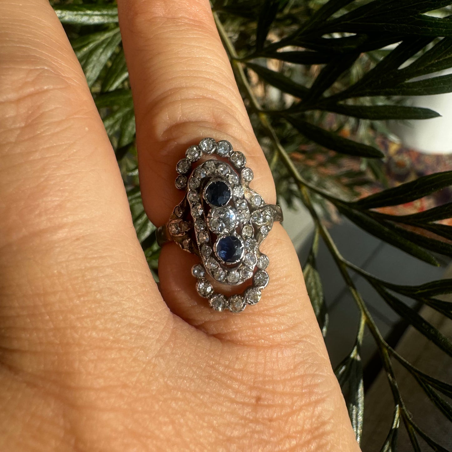 14K gold Antique featuring a stunning trio of gemstones - two deep blue Sapphires surrounding a brilliant old-cut Diamonds