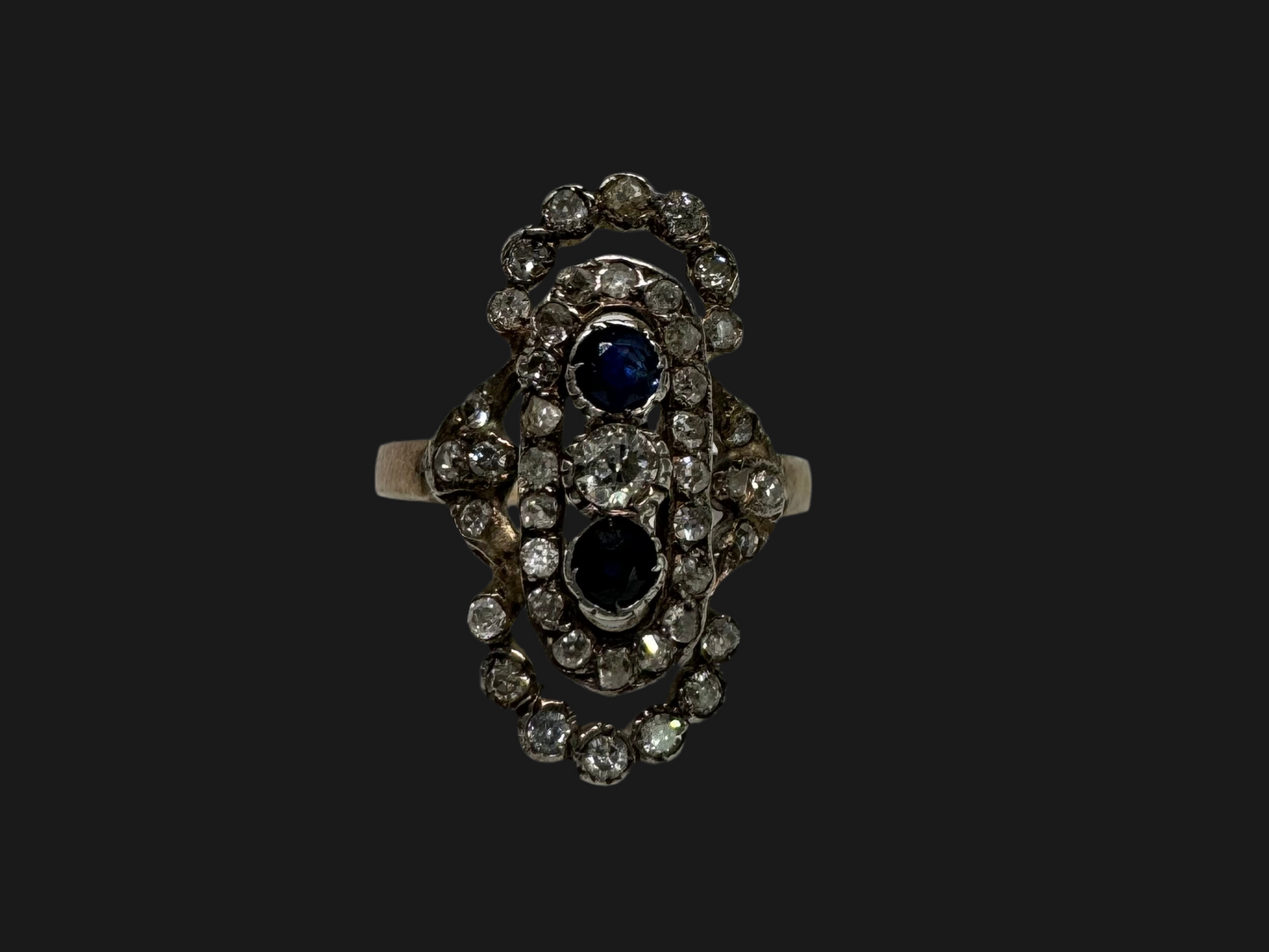 14K gold Antique featuring a stunning trio of gemstones - two deep blue Sapphires surrounding a brilliant old-cut Diamonds