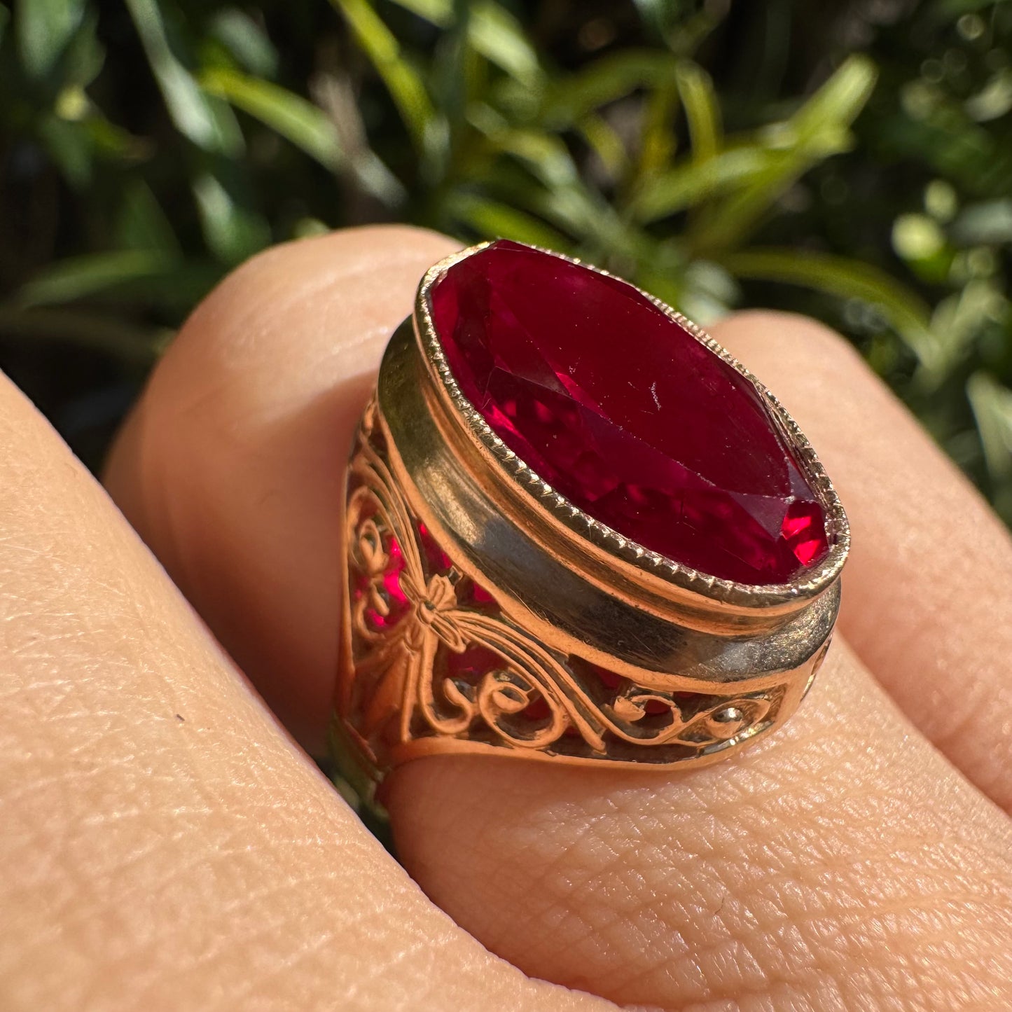 14K gold ring crowned with a vivid oval-cut Ruby, framed in an ornate bezel and accented by intricate filigree details