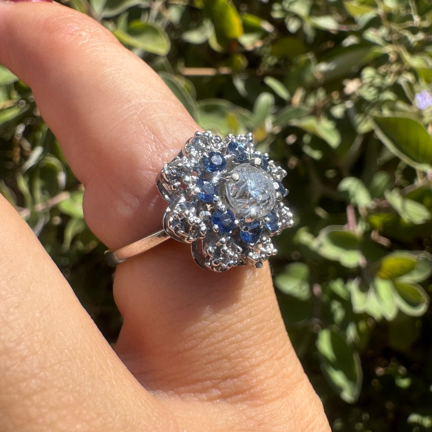 18K gold ring featuring a large round Diamond at the center, surrounded by a floral halo of purple -blue Tanzanite and & Diamonds.