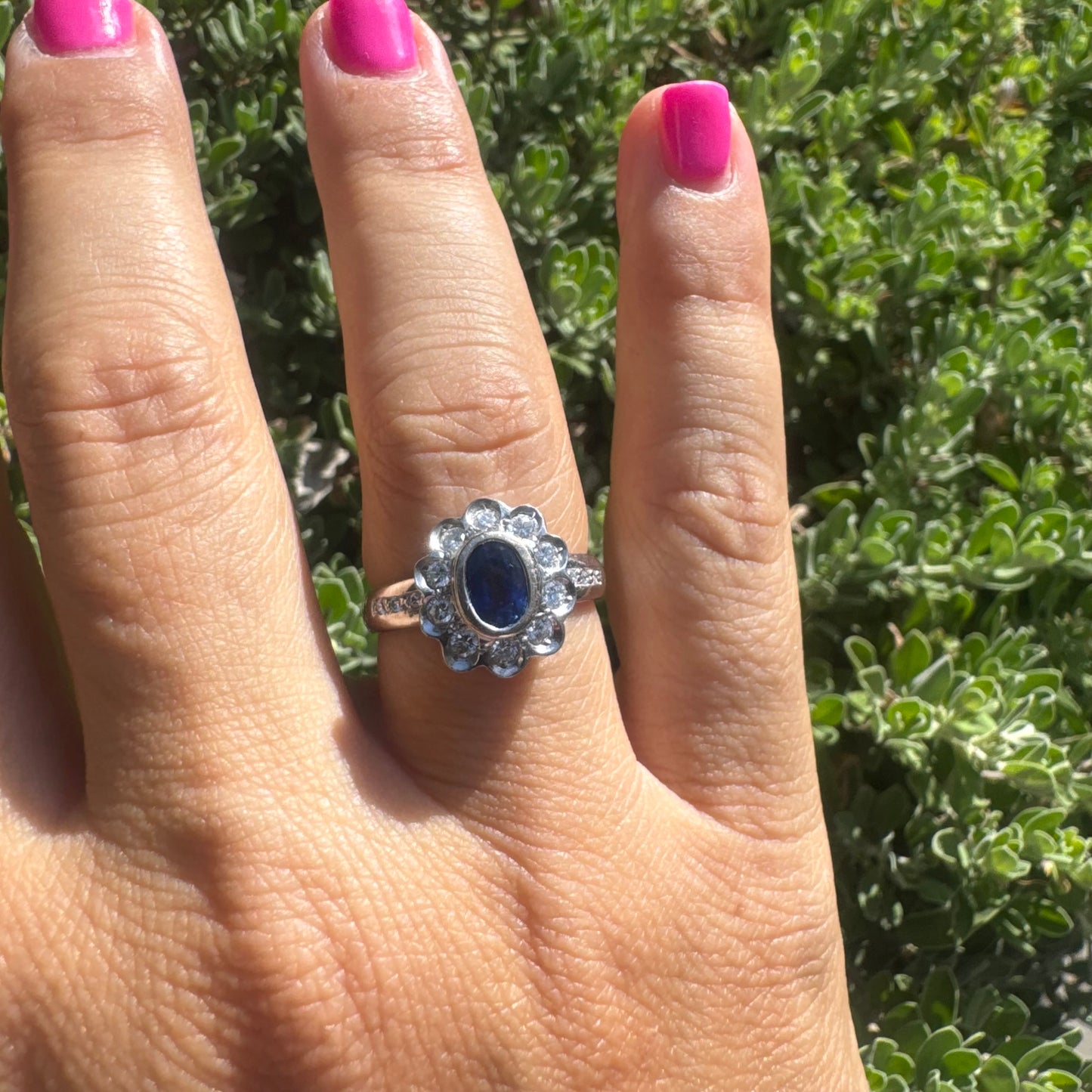 18K gold ring set with an oval blue Sapphire surrounded by a halo of round Diamonds in a flower-shaped design.