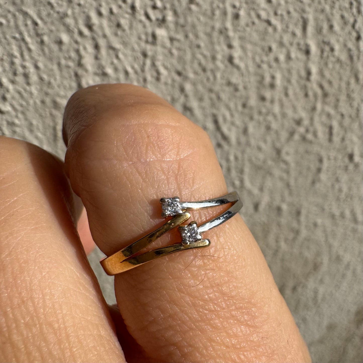 טבעת זהב 14 קראט, עם זרועות מצטלבות בזהב צהוב וזהב לבן, שכל אחת מהן משובצת יהלום קטן ונוצץ.