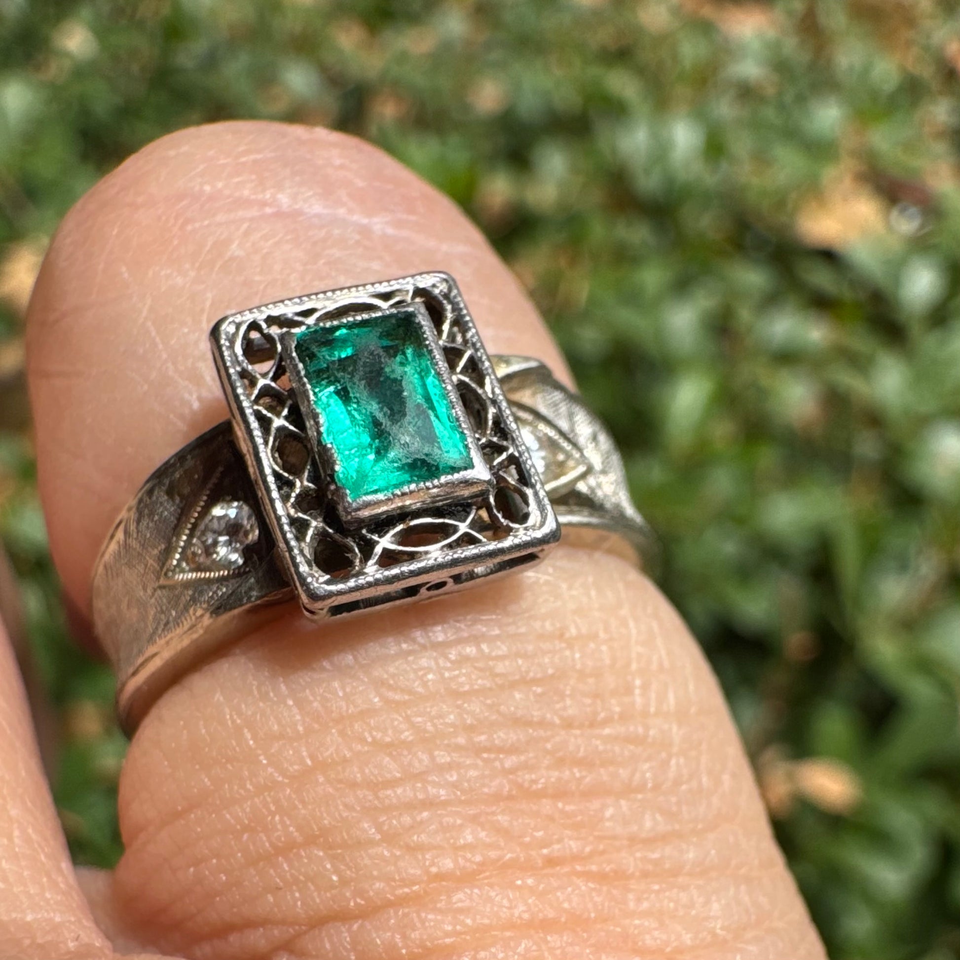 טבעת זהב לבן 14 קראט משובצת אבן אמרלד בחיתוך מלבני (Emerald cut) במרכז, מוקפת במסגרת מלבנית עם עבודת פיליגרן עדינה.