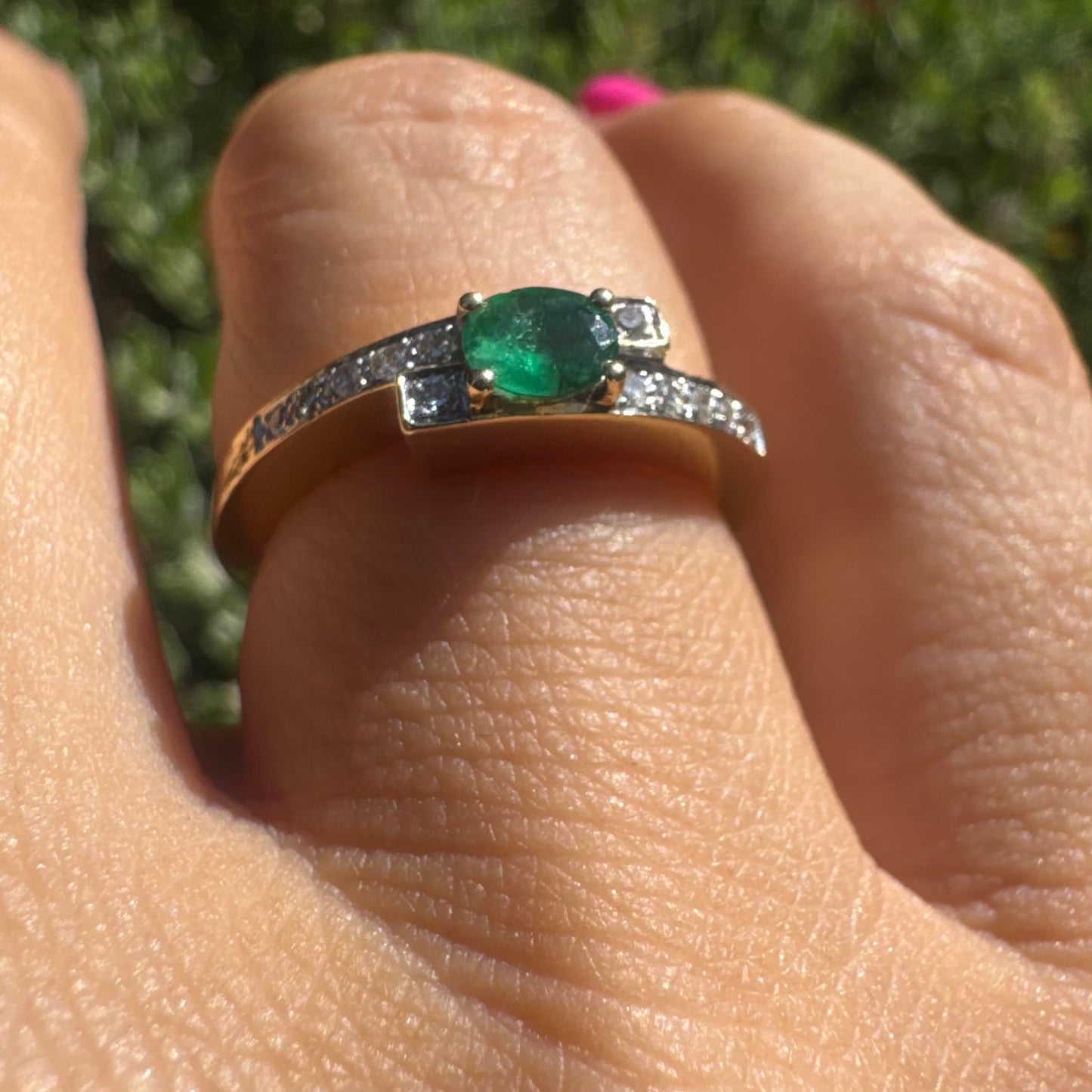 18K gold ring set with an oval green Emerald at the center, accented with sparkling Diamonds along the band.