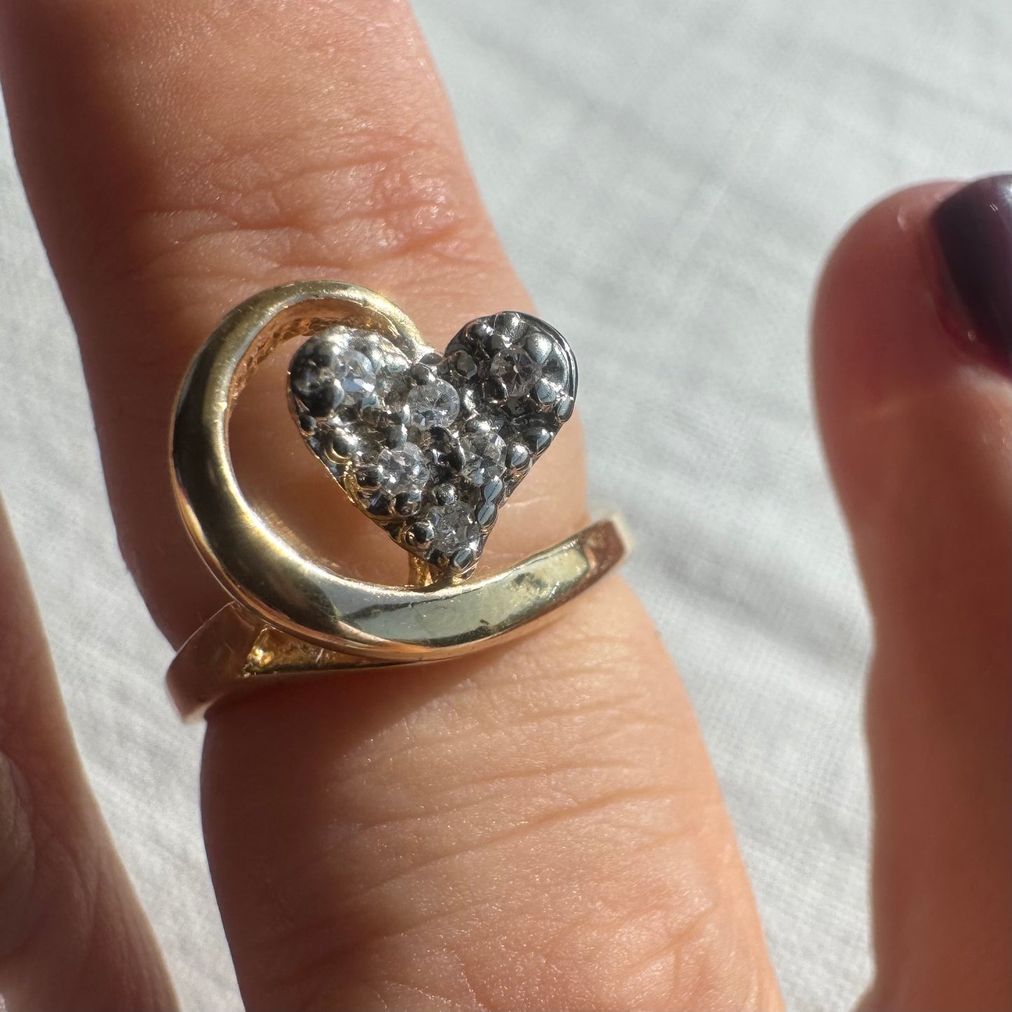 טבעת זהב צהוב 14 קראט ייחודית בעיצוב לב משובץ יהלומים נוצצים, עטופה בקו מוזהב זורם שמעניק תחושת תנועה וחיבוק עדין.