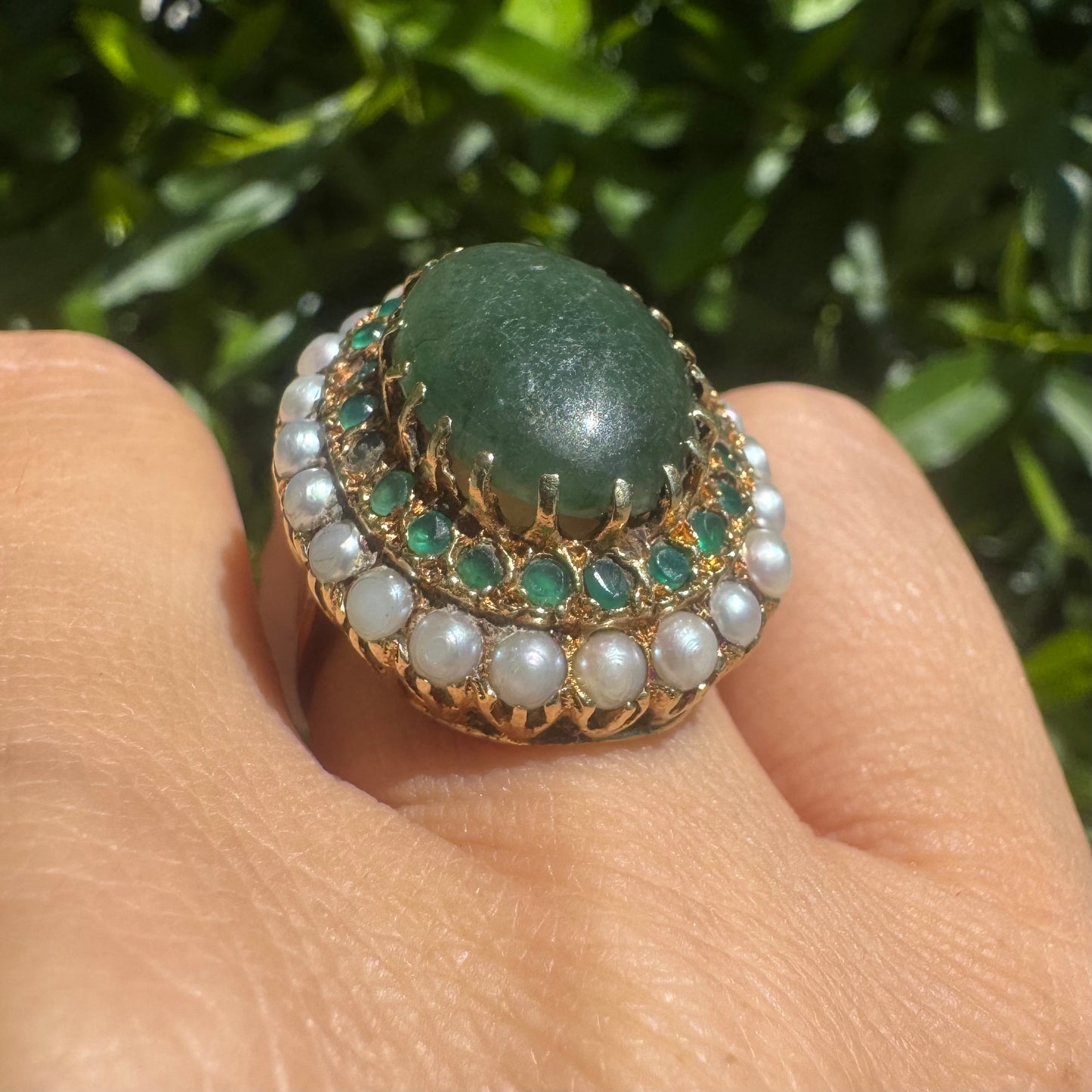 14K gold set with a large oval green Jade at its center, surrounded by concentric halos of sparkling Emeralds and delicate pearls