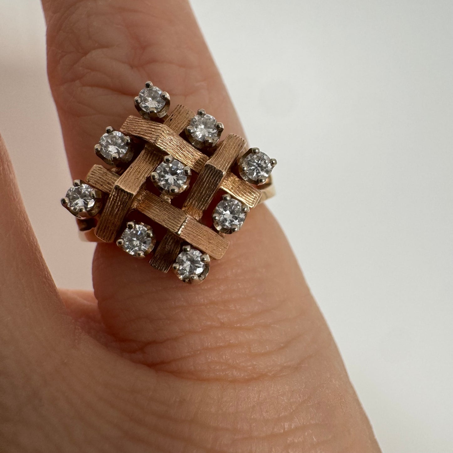 טבעת זהב צהוב 14 קראט בעיצוב קלוע וגאומטרי, משובצת יהלומים עגולים בפריסה סימטרית.