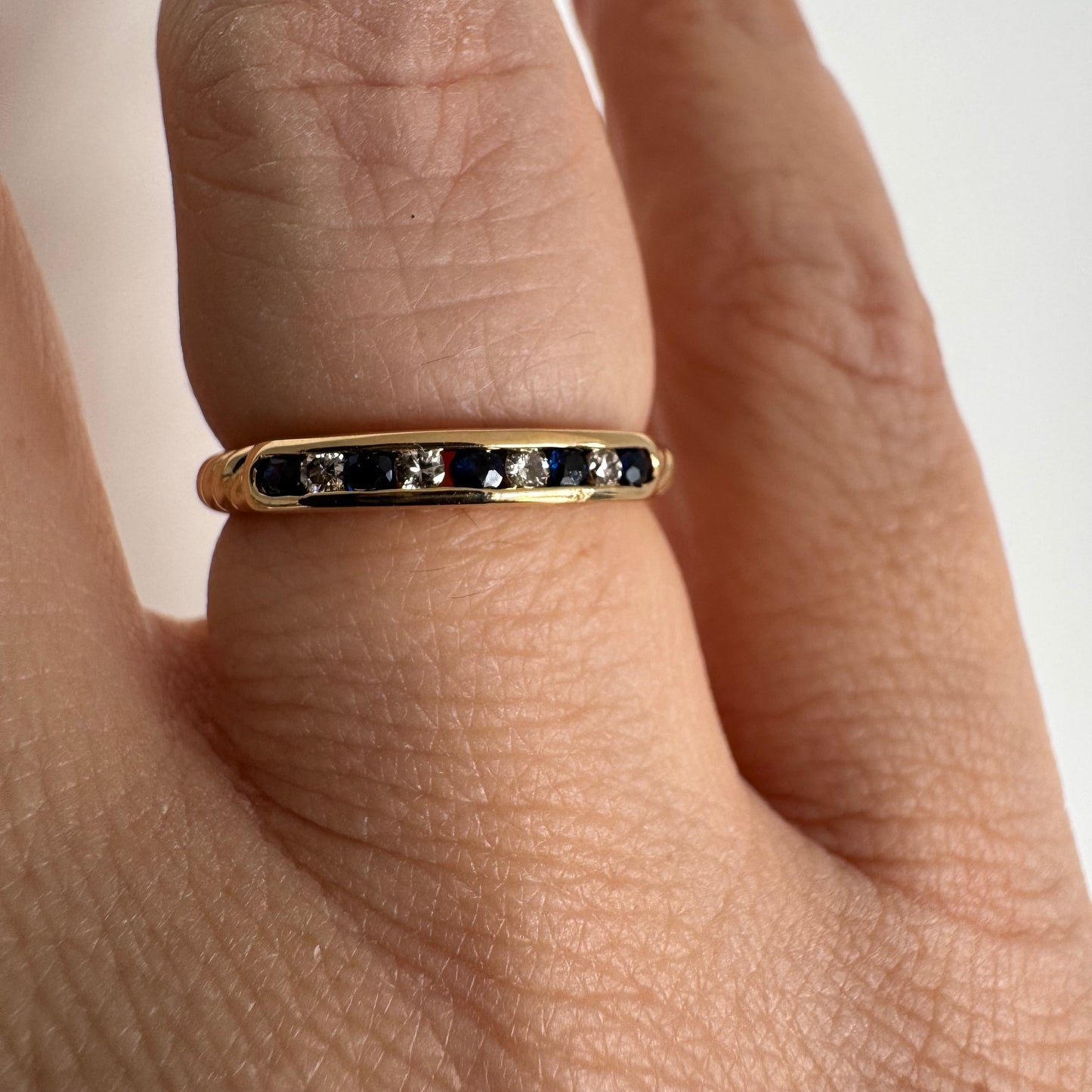 טבעת זהב צהוב 18 קראט בעיצוב נקי ומדויק, משובצת בשורה עדינה של אבני ספיר כחולות וביניהן יהלומים לבנים.
