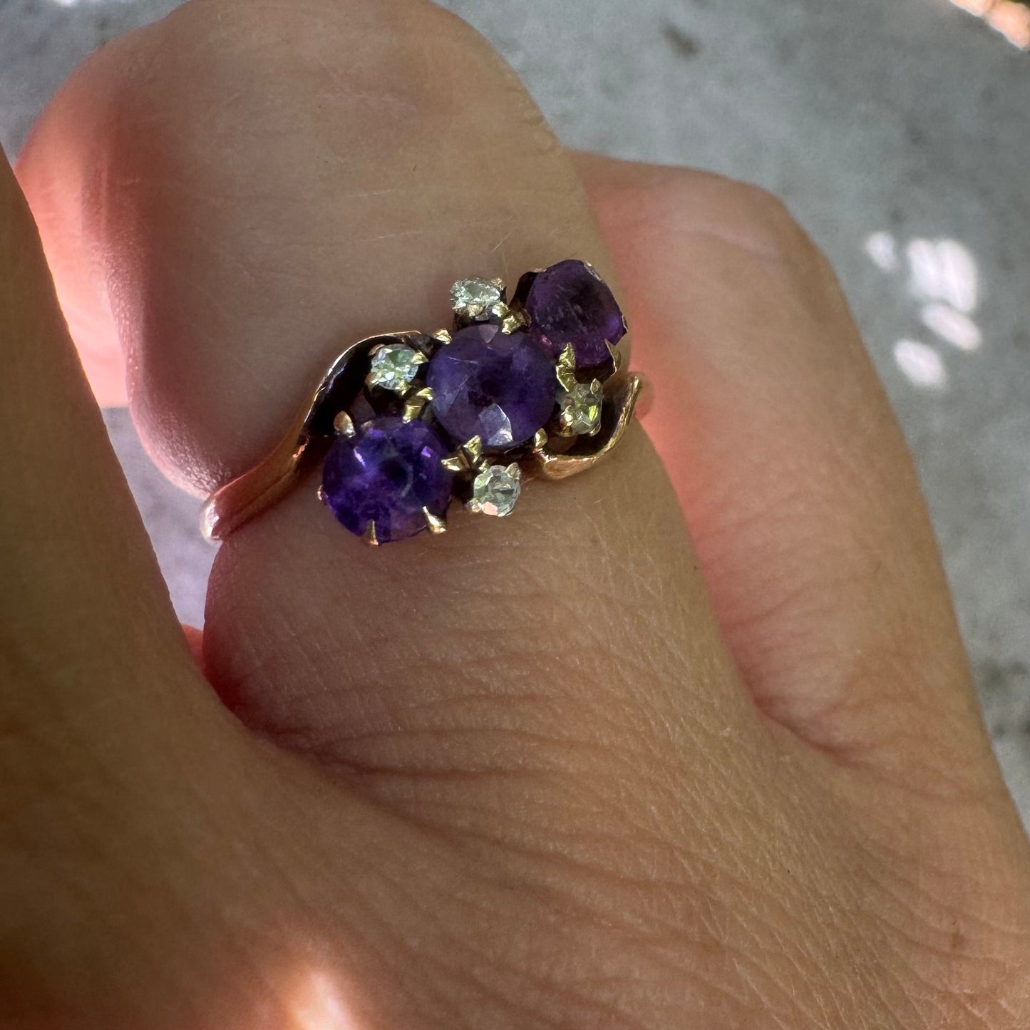 14K gold ring set with three round purple amethysts, accented by small sparkling Diamonds.