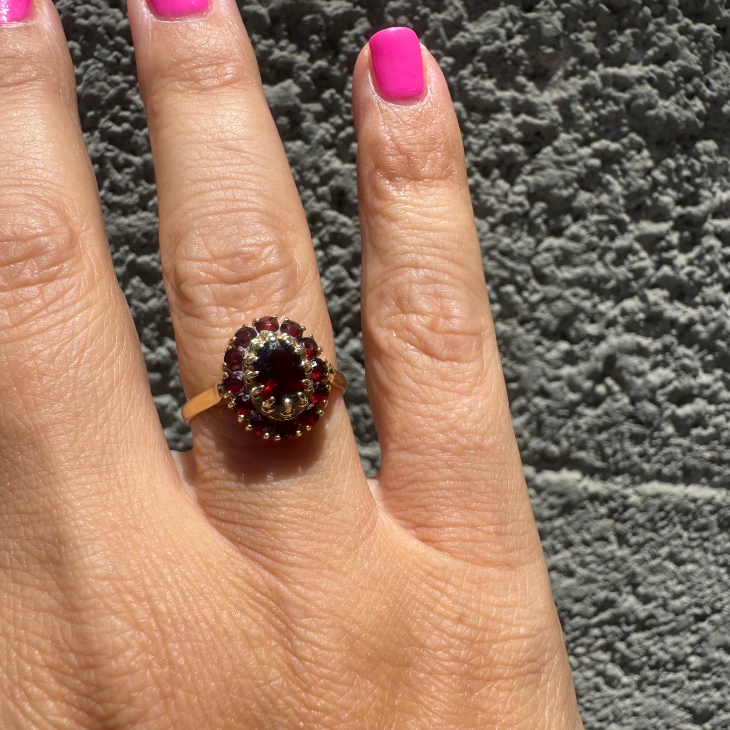 18K gold ring set with an oval garnet center stone, surrounded by smaller garnets