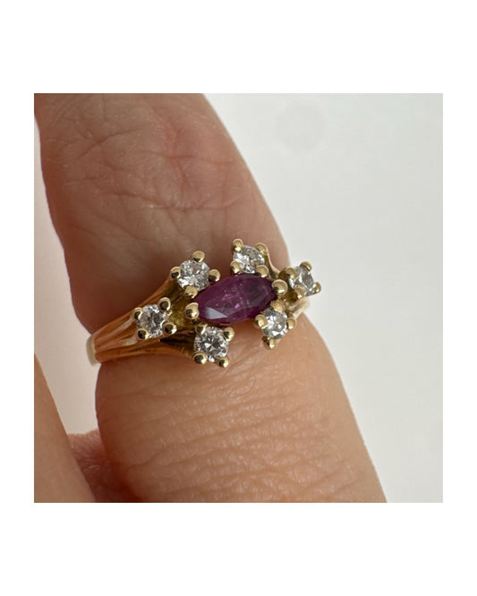 טבעת זהב צהוב 18 קראט משובצת אבן רובי בחיתוך מרקיזה בגוון מוקפת יהלומים בחיתוך עגול משני הצדדים.