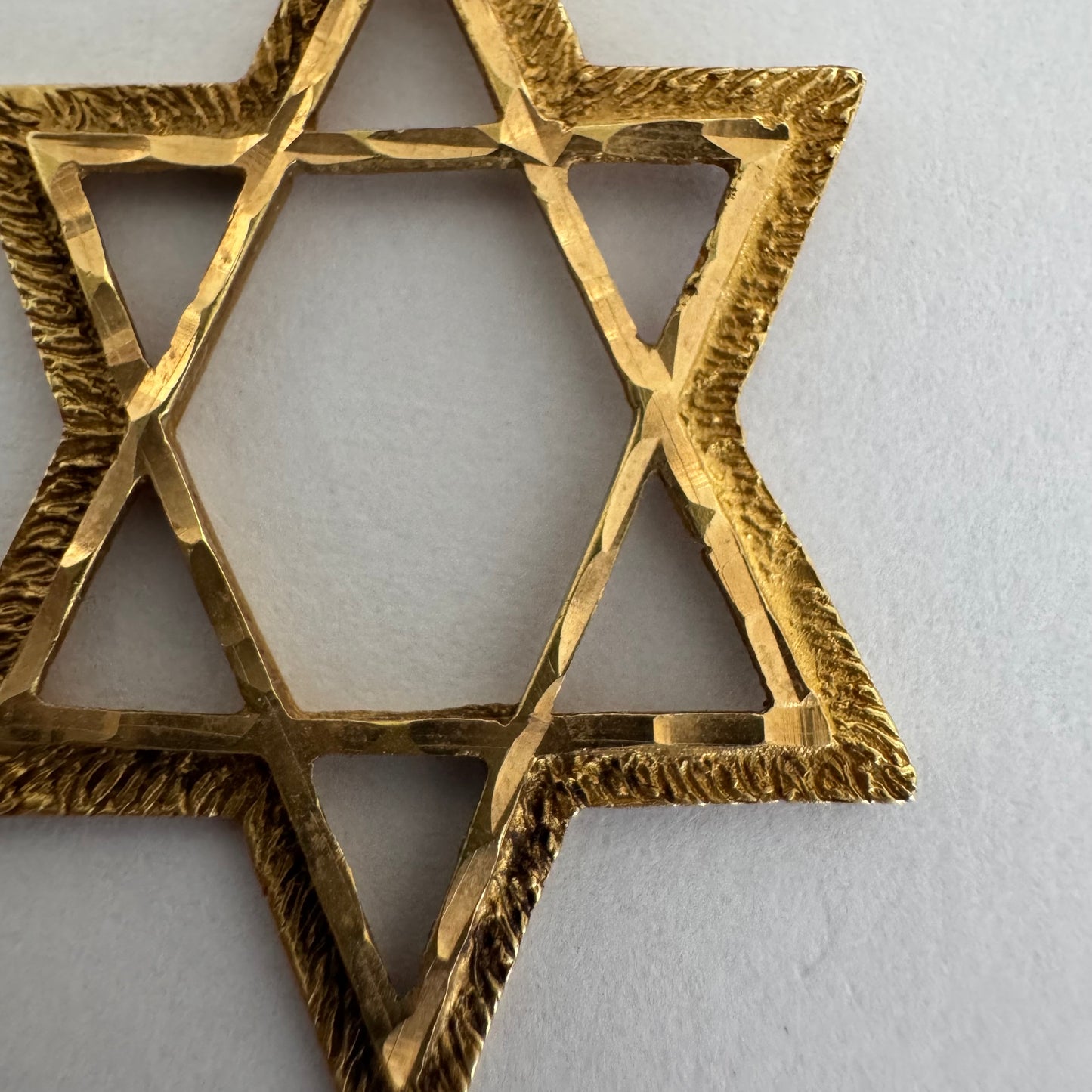 תליון מגן דוד מזהב צהוב 14 קראט בעיצוב פתוח, עם טקסטורה עדינה בשוליים המוסיפה עומק ואופי.
