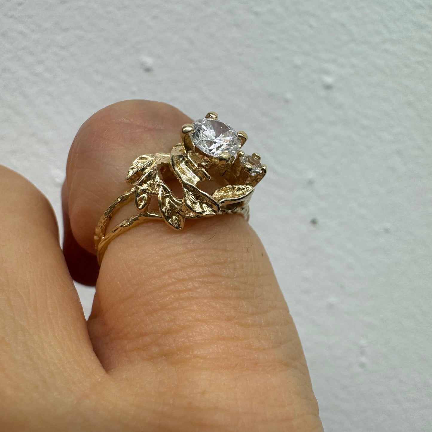 טבעת זהב צהוב 14 קראט בעלת עיצוב אורגני עשיר עם עלים מגולפים סביב שלוש אבנים שקופות נוצצות. (לא יהלומים)